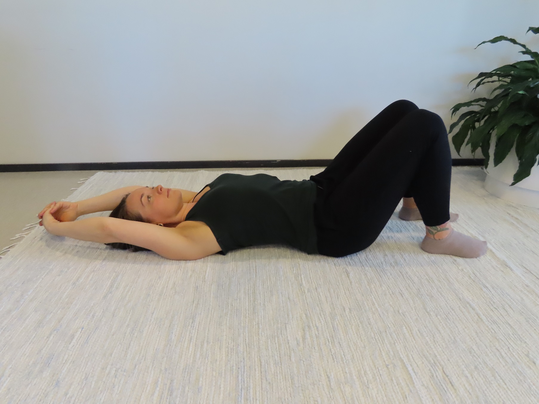 Kvinnan ligger på rygg på golvet, med böjda knän, fingrarna korsade och armarna sänkta bredvid huvudet.