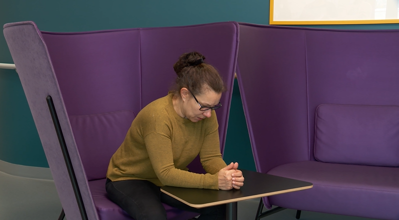 Nainen istuu ja nojaa kyynärvarsilla pöytään.