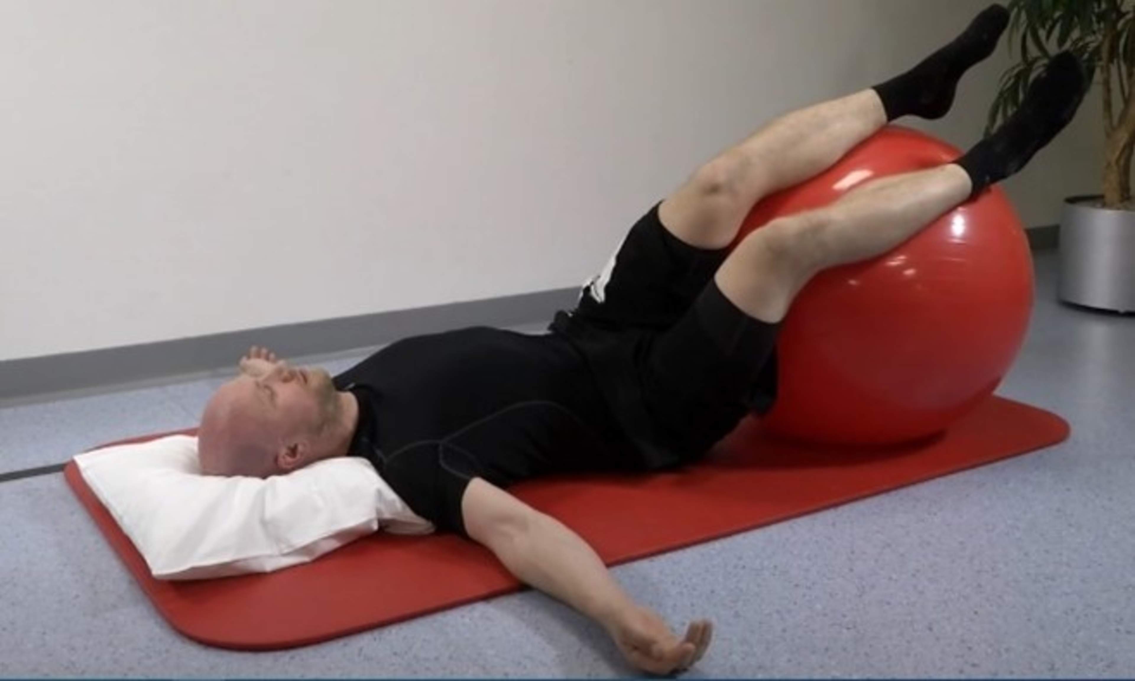 Mies makaa lattialla jalat jumppapallon päällä ja on vienyt jalkoja toiselle puolelle, jolloin selkä kiertyy.