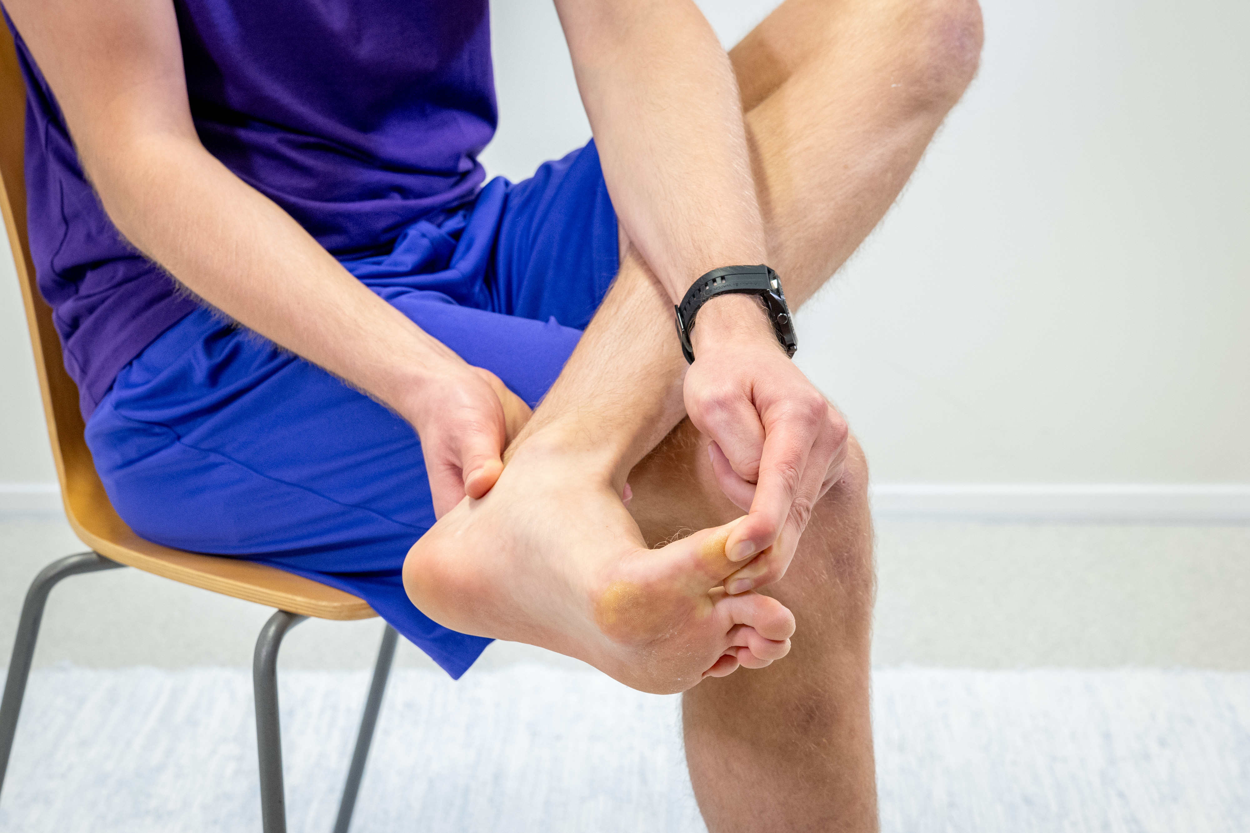 Mies istuu tuolilla oikea nilkka nostettuna vasemman polven päälle. Mies pitää oikealla kädellä kiinni nilkasta ja vasemmalla kädellä venyttää eli nostaa isovarvasta ylöspäin. 