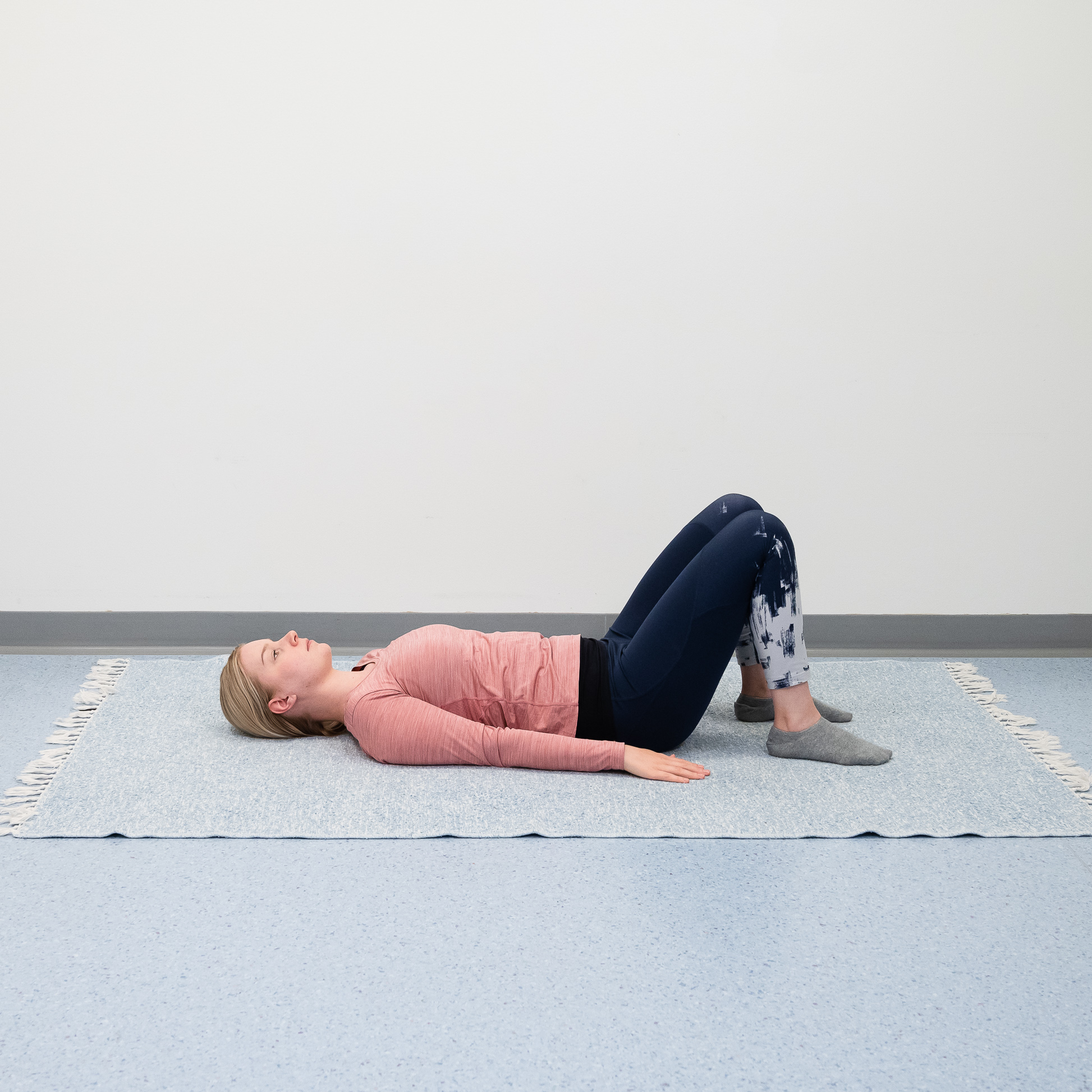 Nainen makaa selällään lattialla polvet koukussa ja jalkapohjat lattiassa.