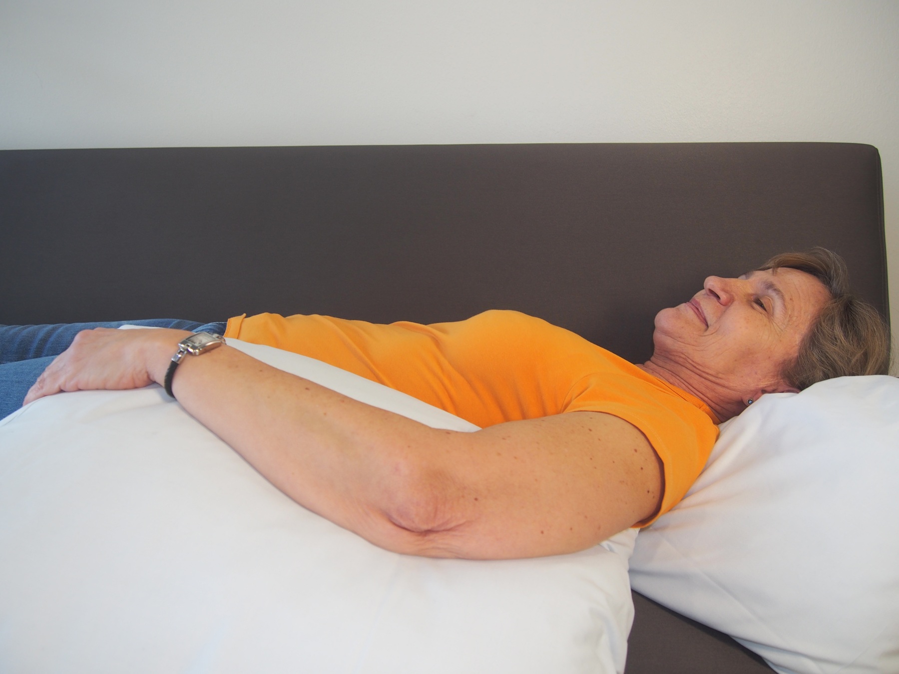 Kvinnans arm är upphöjd i högläge på kuddar när hon ligger på rygg.