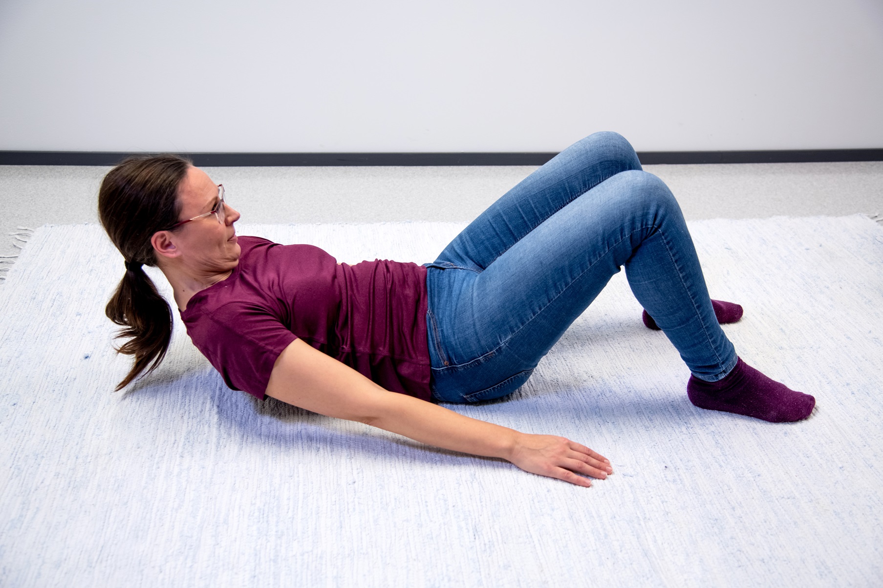 Nainen makaa lattialla selinmakuulla polvet koukussa ja jalkapohjat lattiassa. Nainen on nostanut hartiat ja pään irti lattiasta. Kädet ovat vartalon vierellä. 