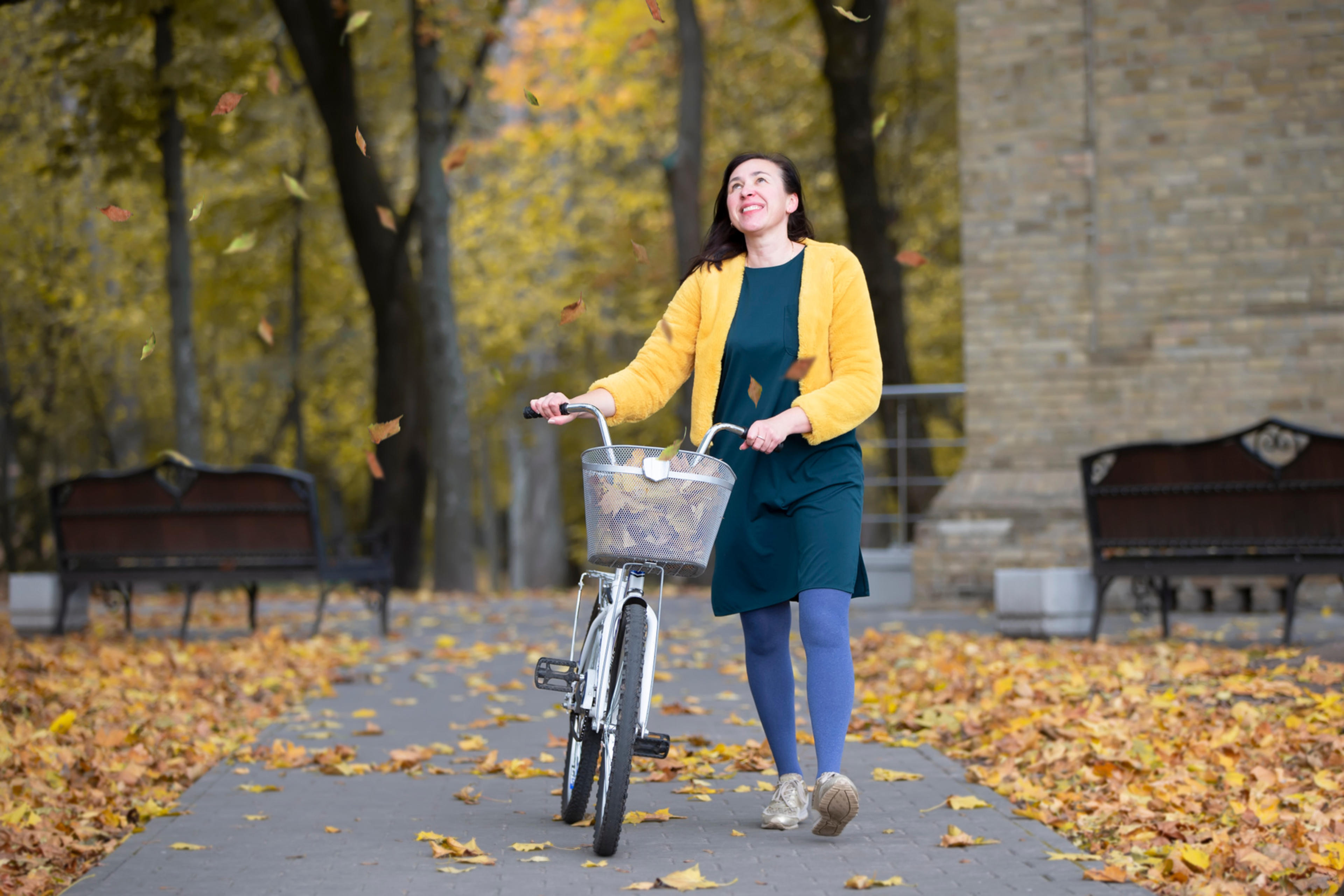 En medelålders kvinna leder en cykel på en höstig gata.