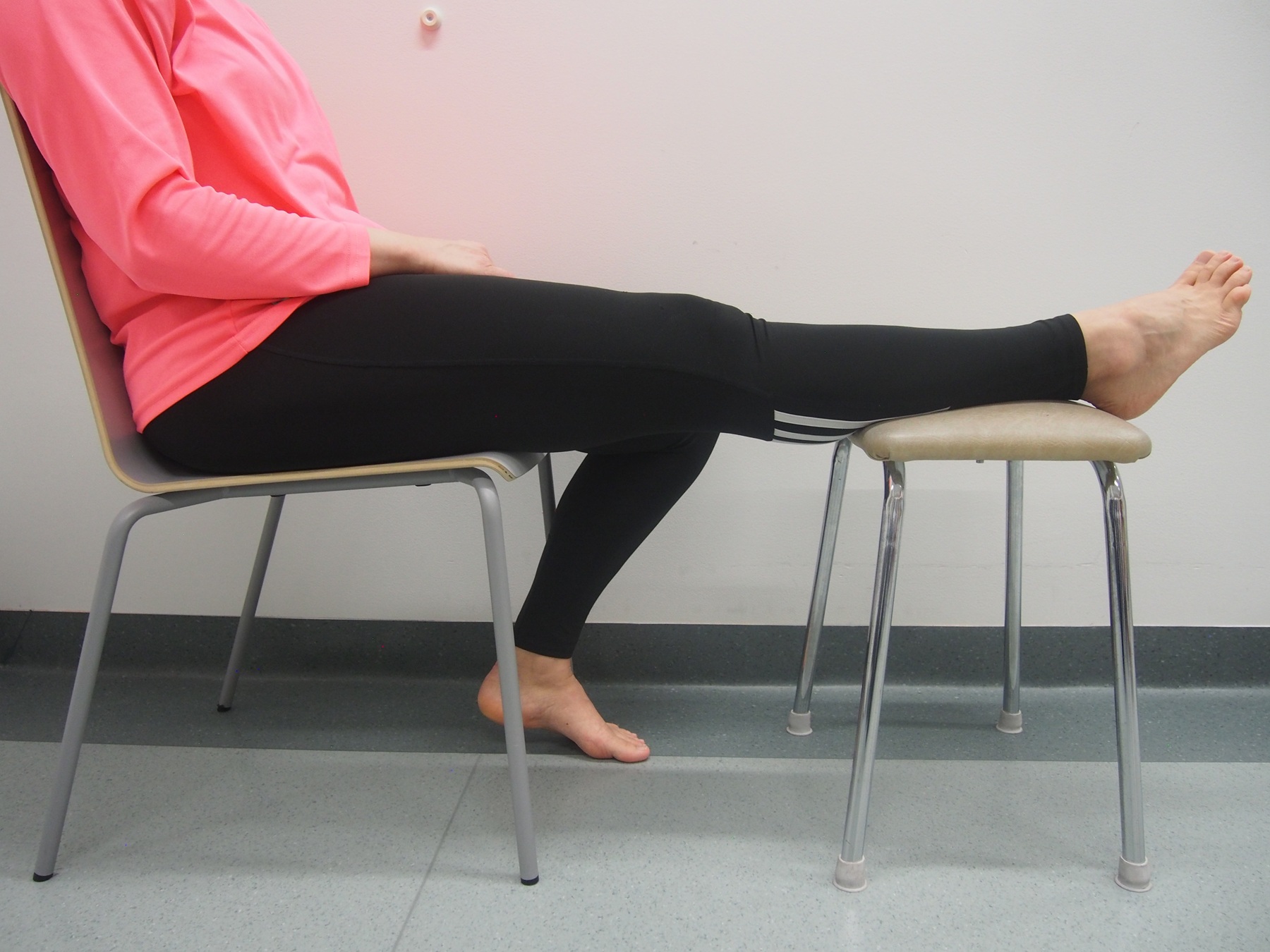 Nainen istuu ja toinen jalka on kohoasennossa nostettuna tuolille.