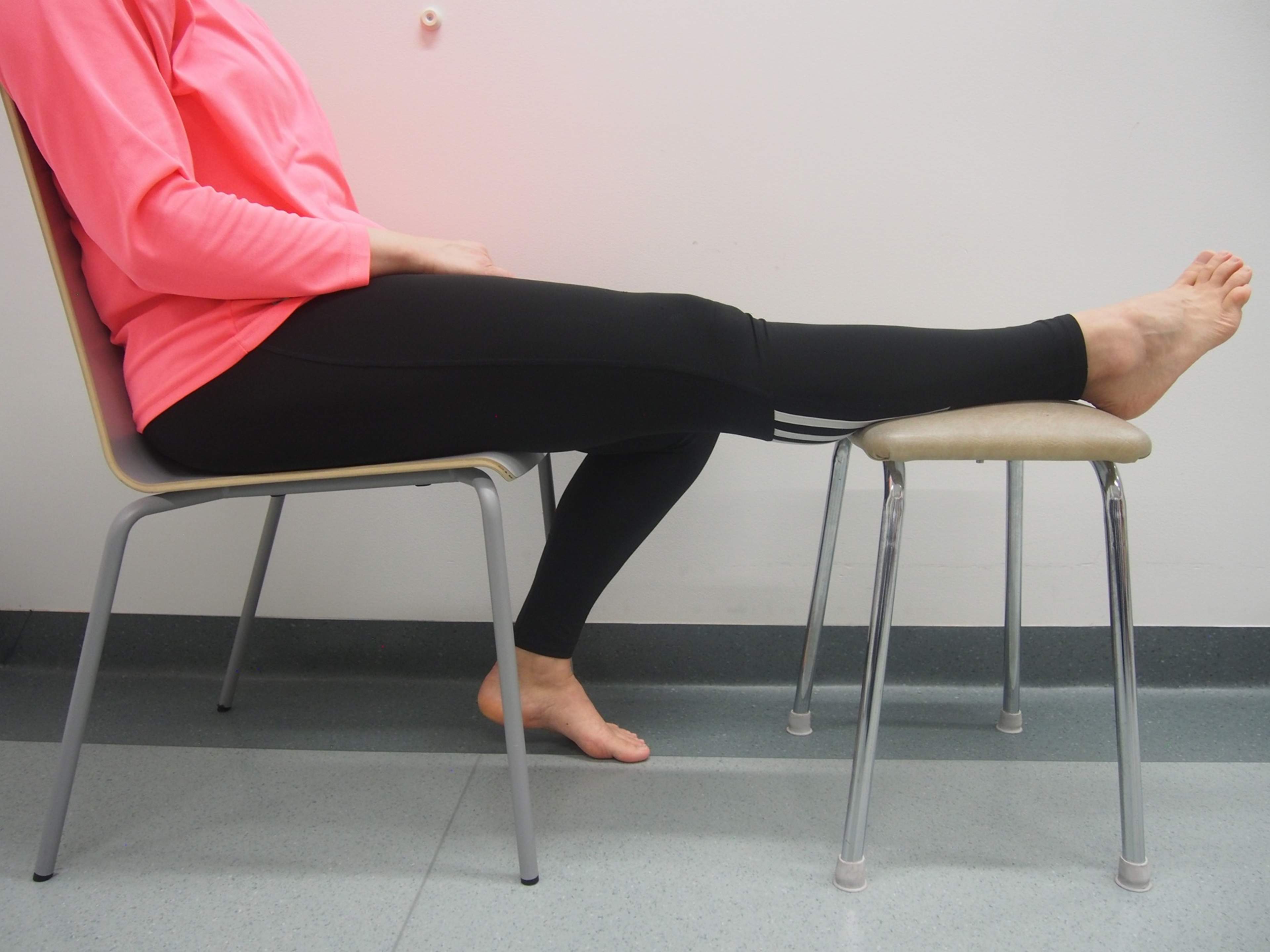 Nainen istuu ja toinen jalka on kohoasennossa nostettuna tuolille.