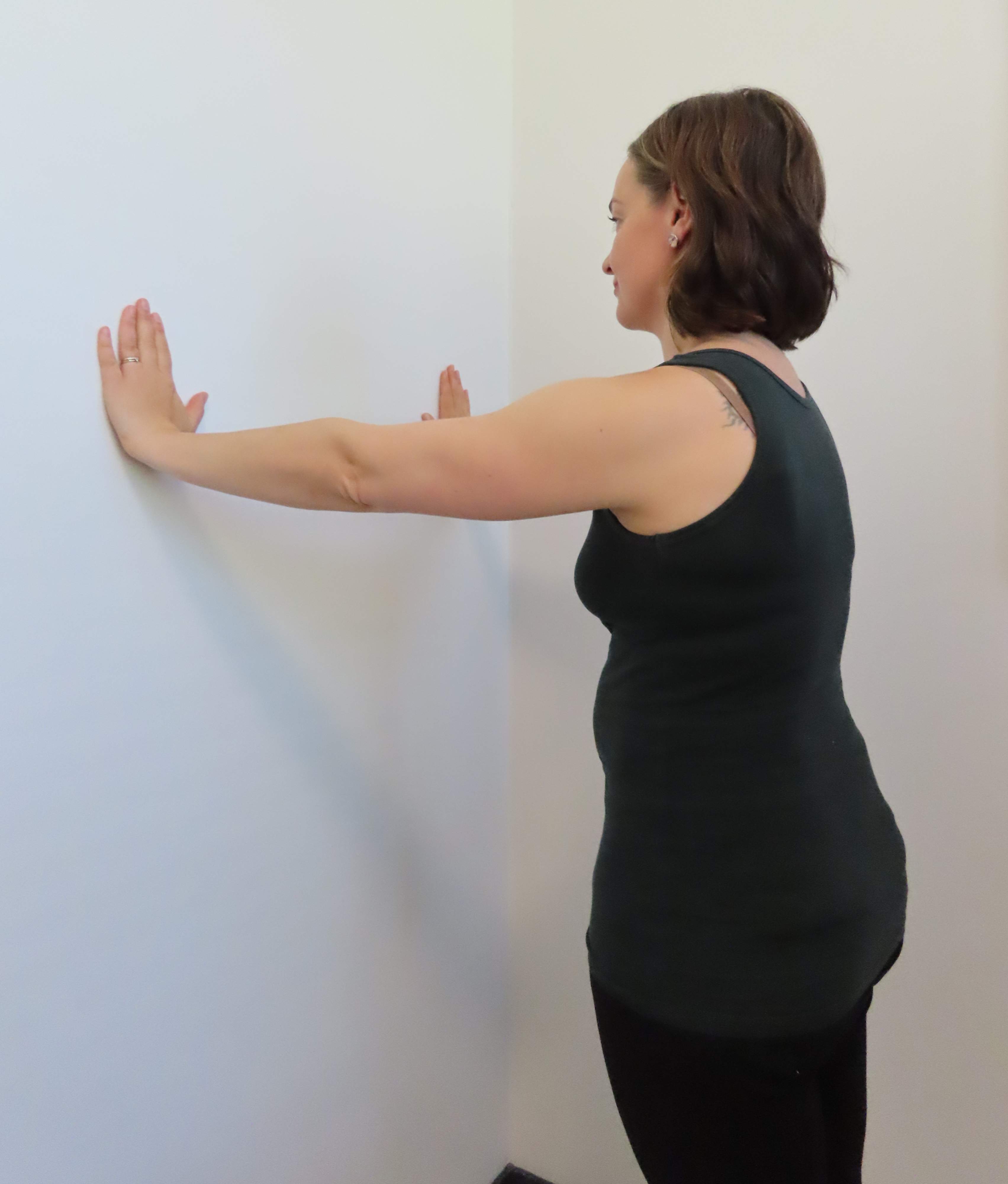 Kvinnan står vänd mot väggen med händerna i en bred armhävningsposition mot väggen i brösthöjd, så att fingrarna pekar uppåt.