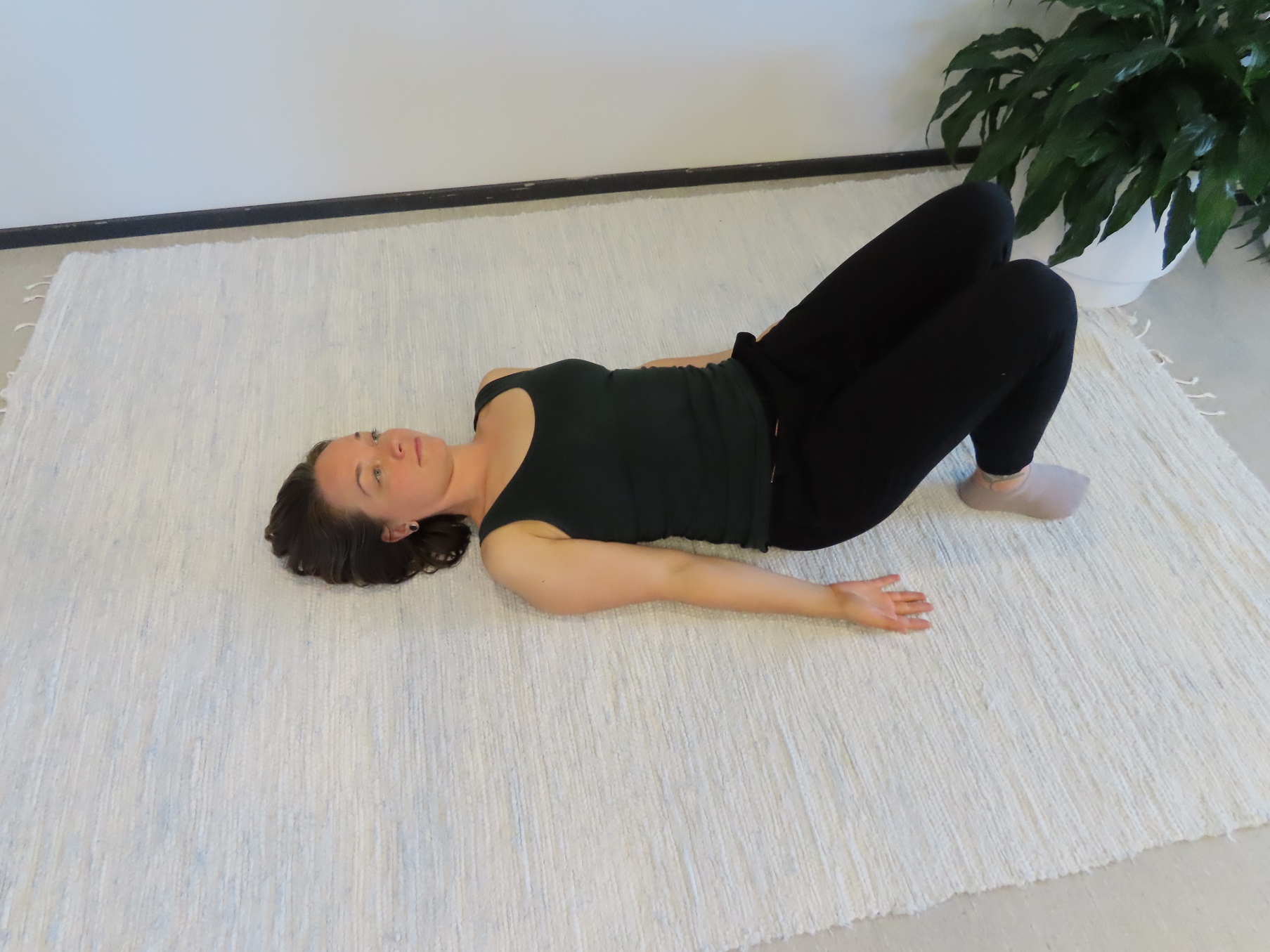 Nainen makaa selinmakuulla lattialla, polvet koukussa ja kämmenselät lattiaa vasten vartalon vierellä.