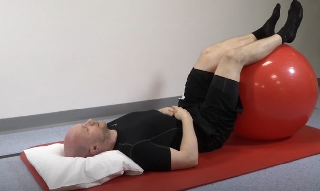 Mies makaa lattialla jalat jumppapallon päällä.