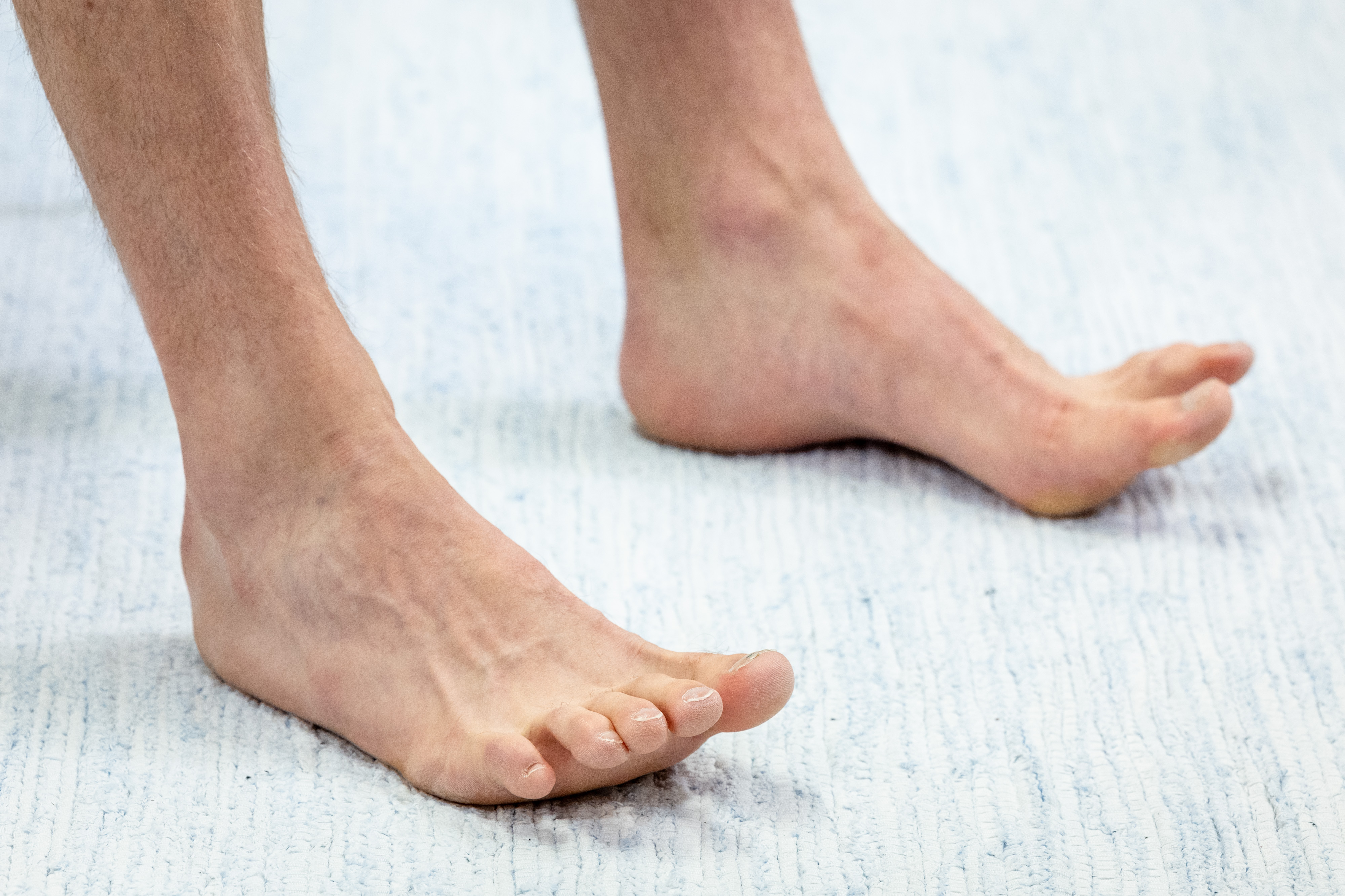 Miehen paljas jalkapohja on lattialla maton päällä. Mies on nostanut varpaat ylös. Kantapää ja päkiät pysyvät kiinni lattiassa. 