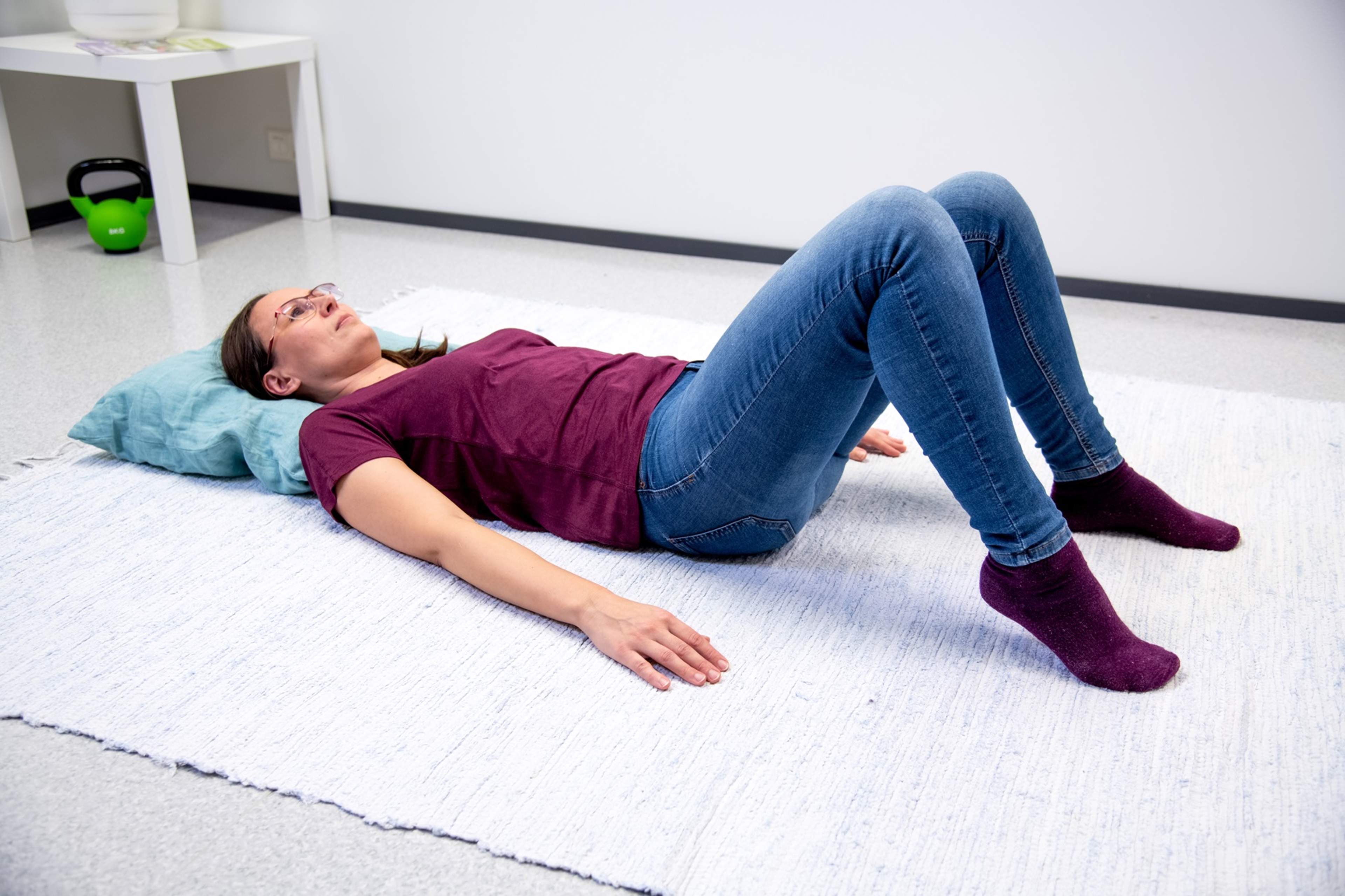 Nainen makaa lattialla selällään polvet koukussa ja jalkapohjat lattiassa. Toinen kantapää on nostettuna ilmaan.