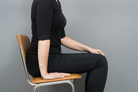 En kvinna sitter på en stol handen bredvid kroppen på sitsen.