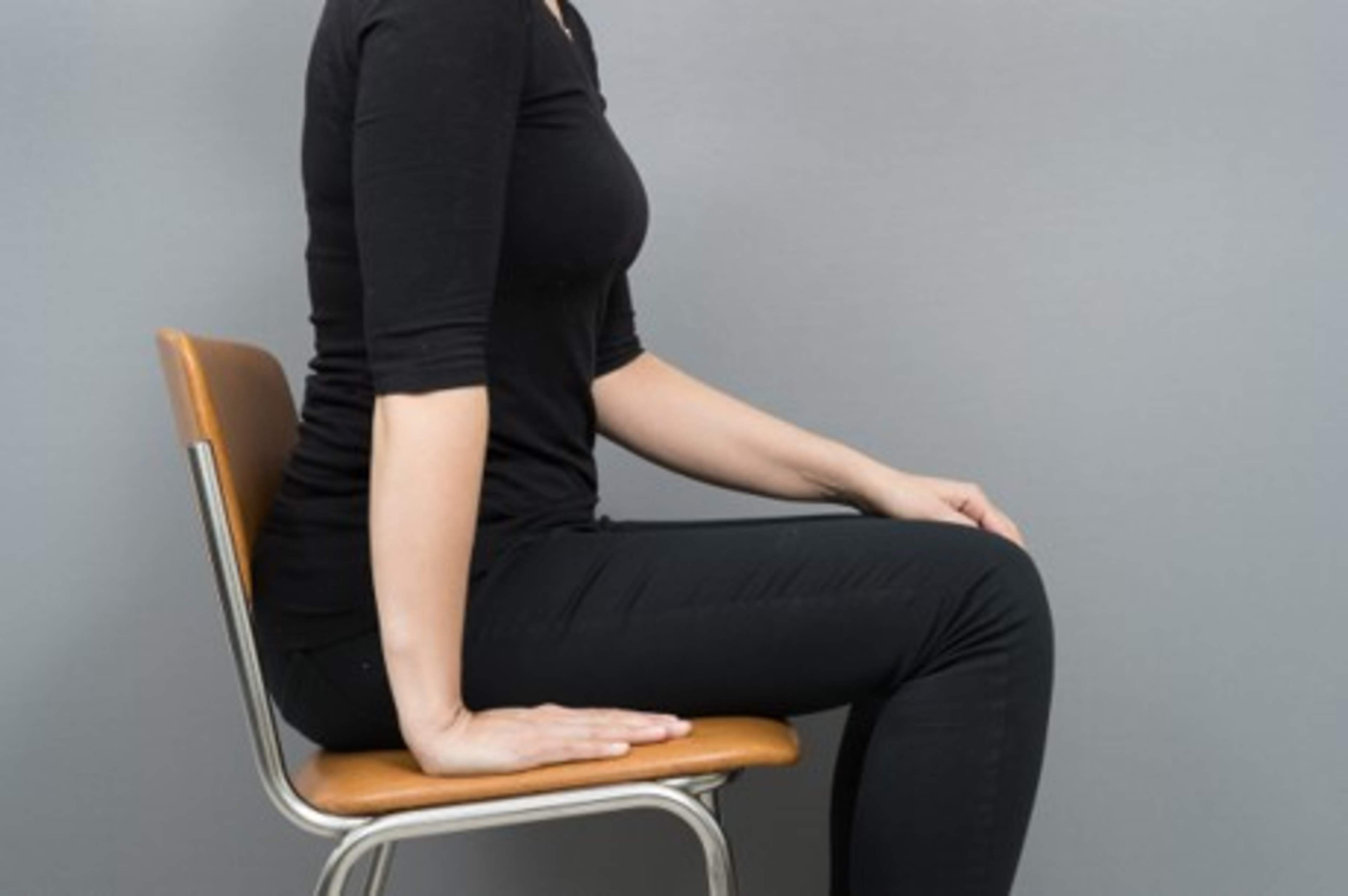 Nainen istuu käsi vartalon vierellä tuolilla.
