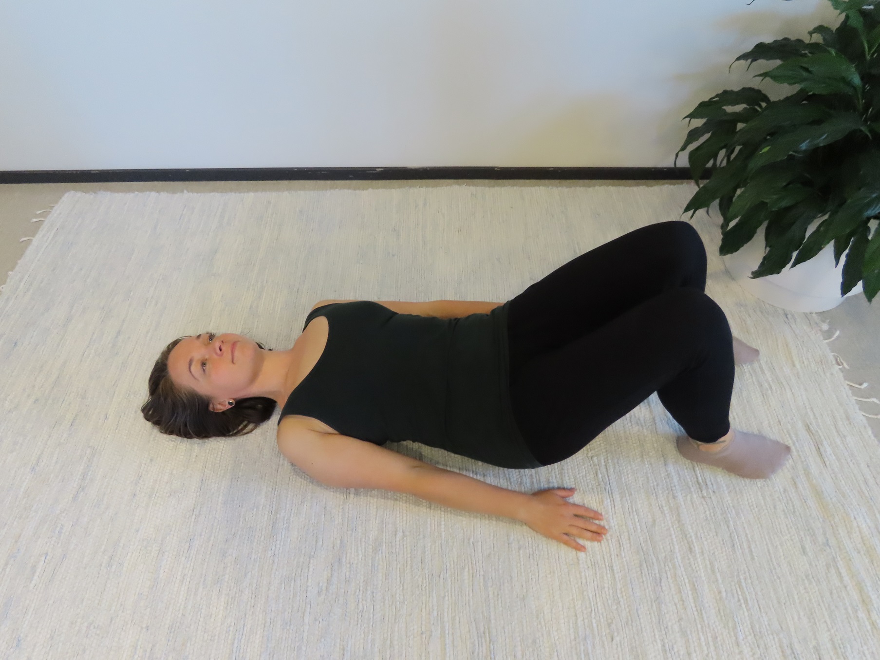 Nainen makaa selinmakuulla lattialla, polvet koukussa ja kädet vartalon vierellä.