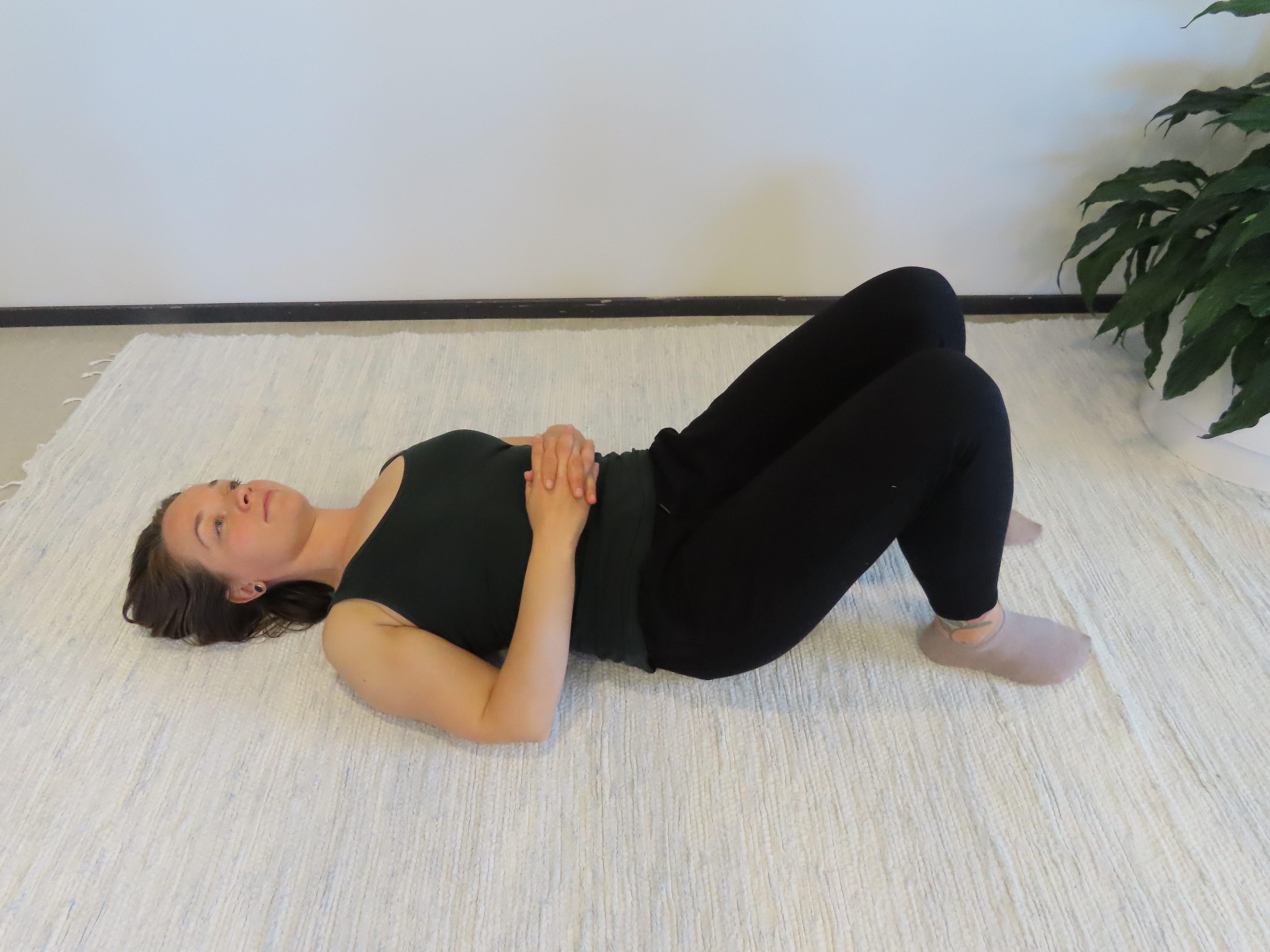 Nainen makaa selinmakuulla lattialla, polvet koukussa ja sormet ristissä vatsan päällä.