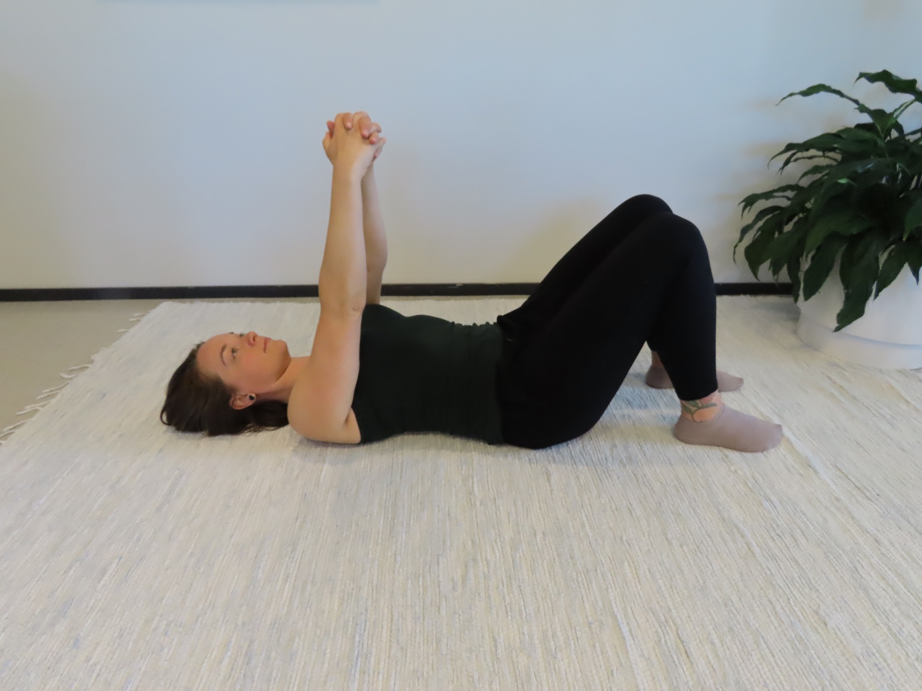 Nainen makaa selinmakuulla lattialla, polvet koukussa, sormet ristissä ja kädet nostettuna ylös.