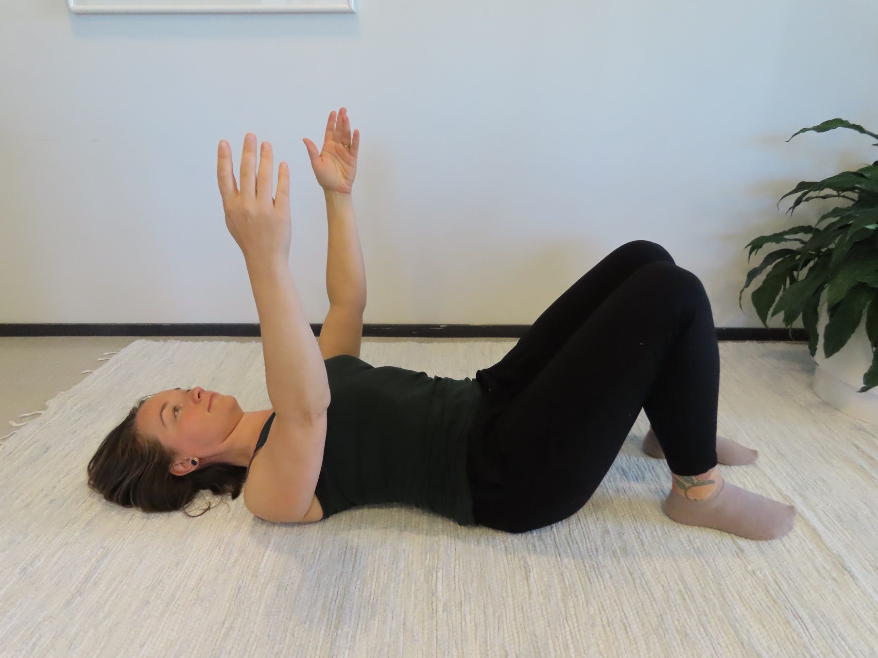 Kvinnan ligger på rygg på golvet, med böjda knän och armarna sträckta upp mot taket.