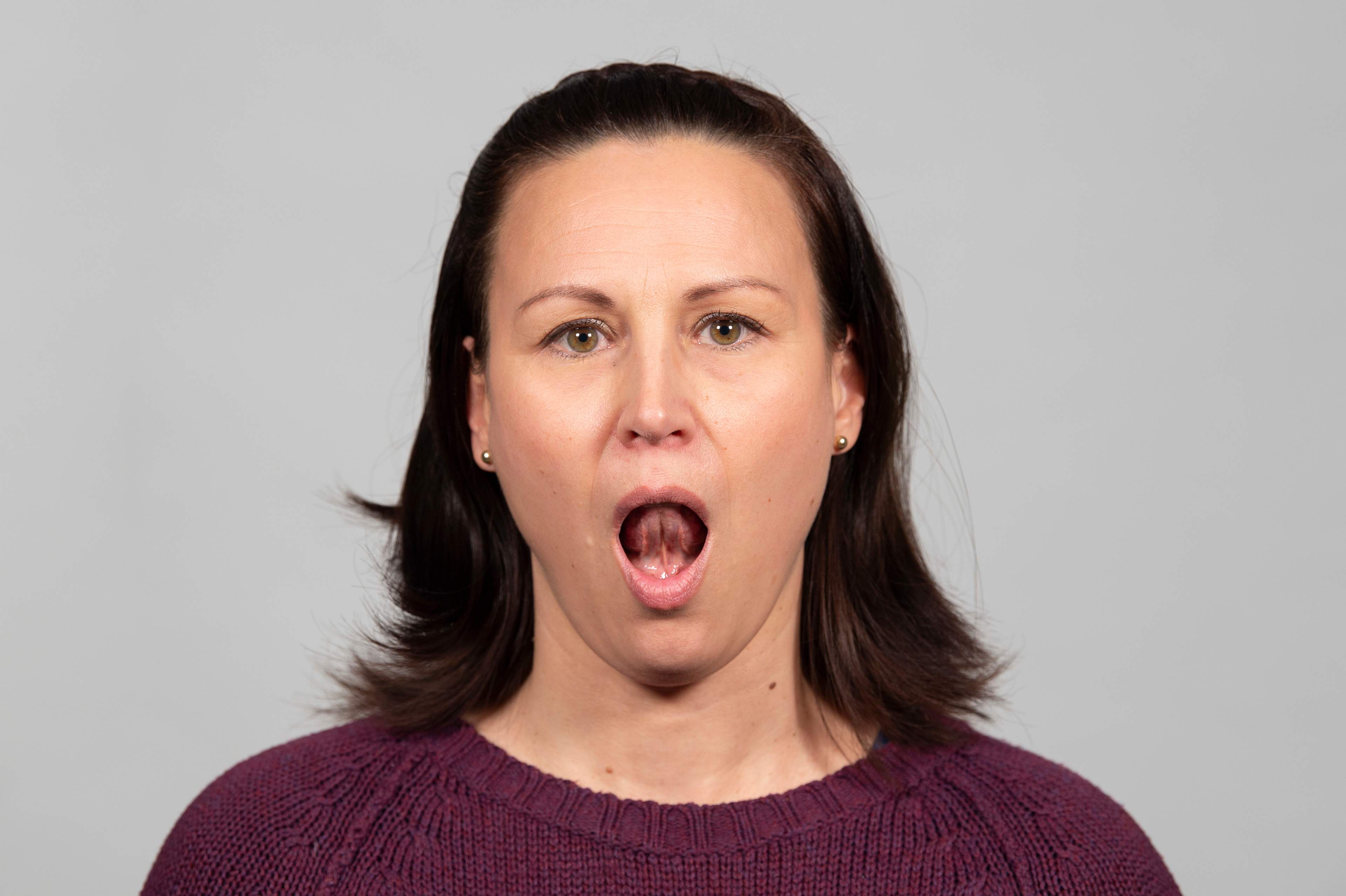 Kvinna har munnen stort öppnad med tungan placerad bakom de övre framtänderna.