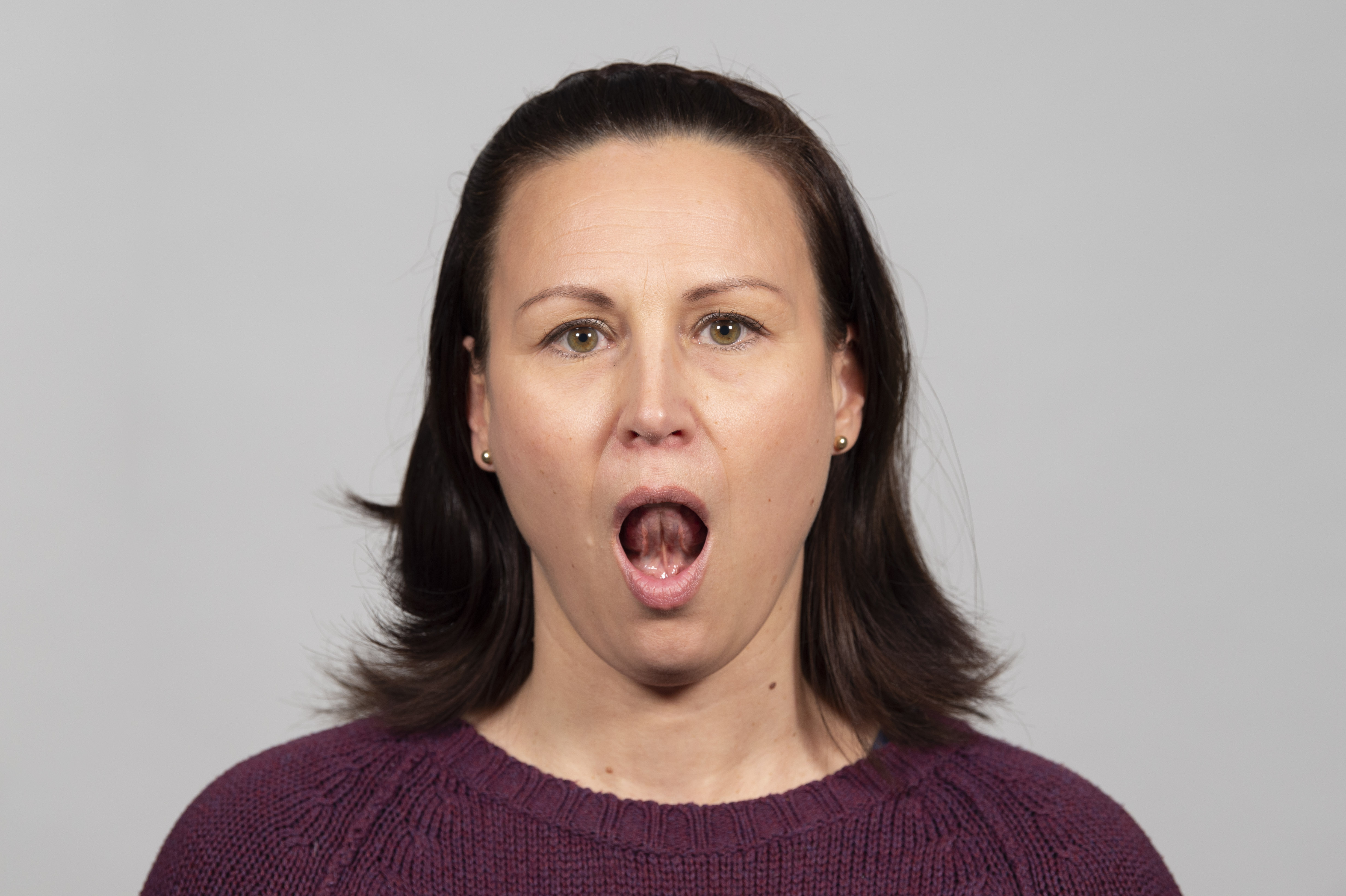 Nainen on suu avattuna suuresti auki kieli yläetuhampaiden takana. 