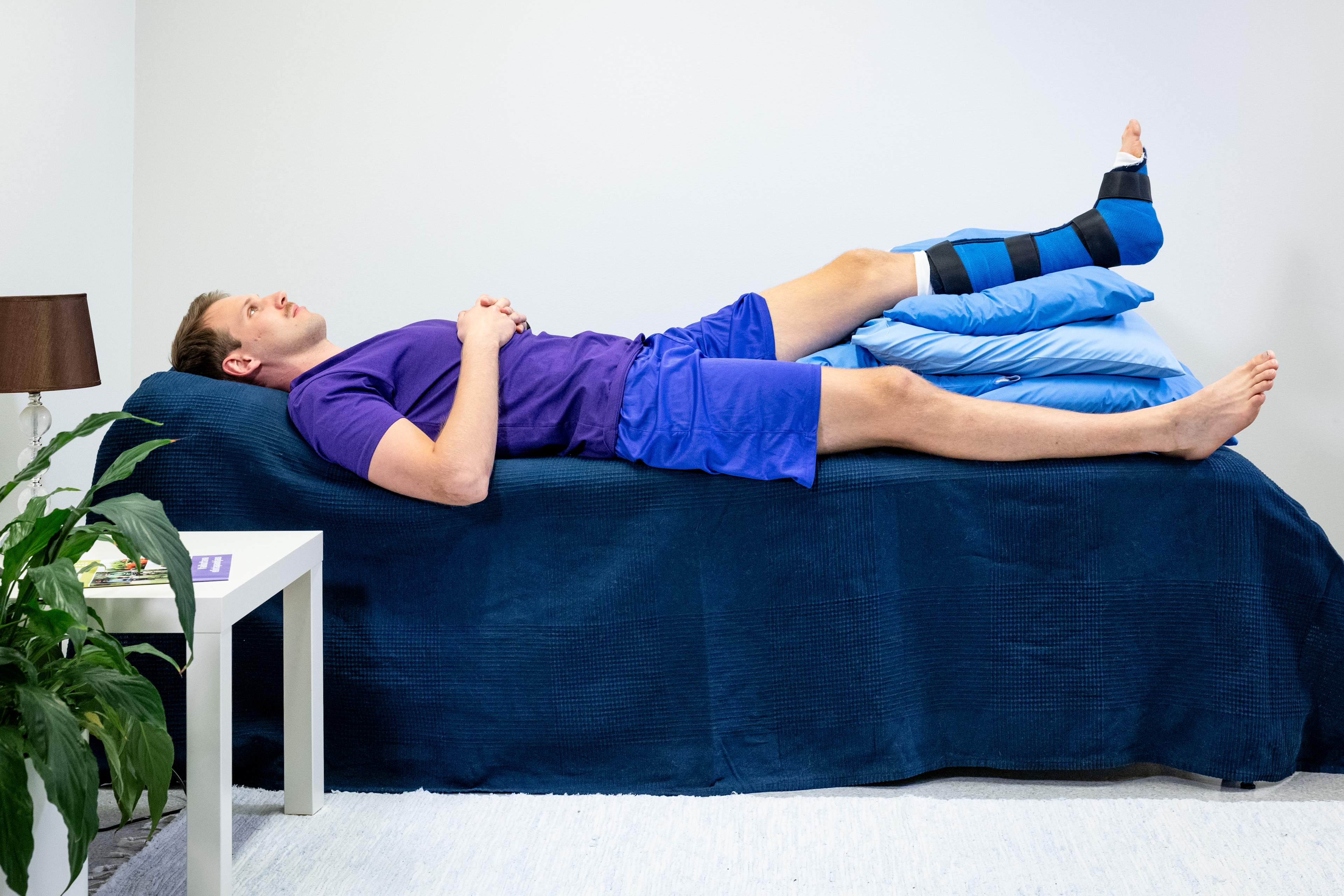 Mies makaa selällään sängyllä, vasemman jalan nilkassa on kipsi ja jalka on nostettu tyynyjen päälle.