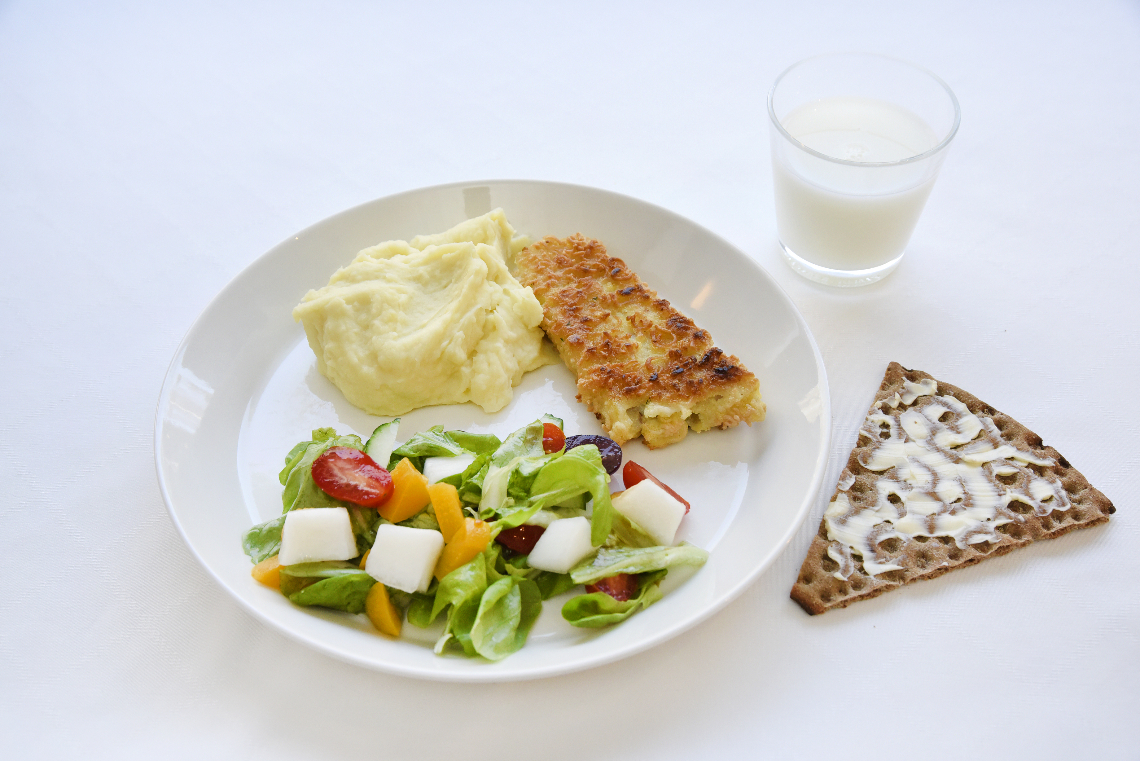 På tallriken finns hälften sallad, en fjärdedel potatismos och en fiskbiff. Som måltidsdryck finns ett glas mjölk och som tilltugg en bit knäckebröd med smör.