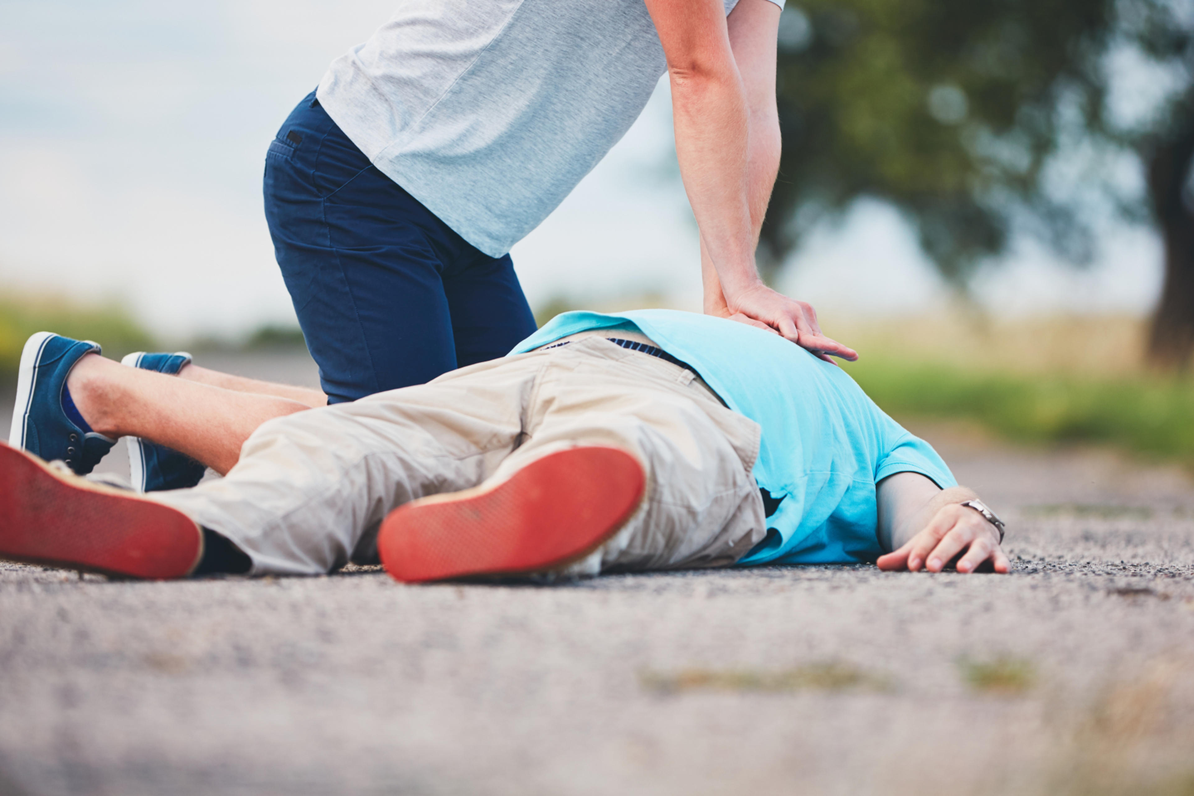A helper kneeling and giving CPR to a person collapsed in the street.