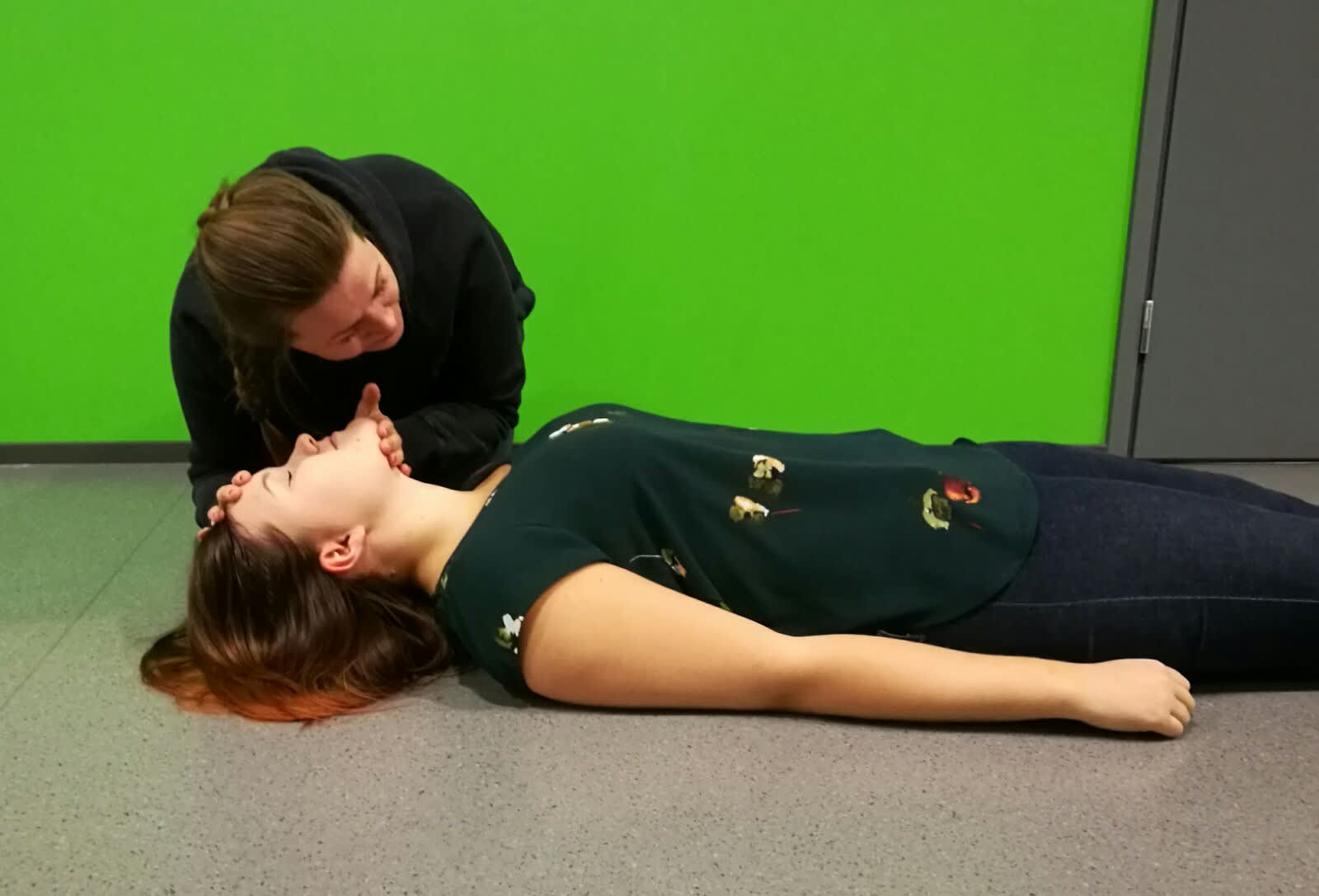 A helper monitors an unconscious person’s airway by monitoring the movement of their chest.
