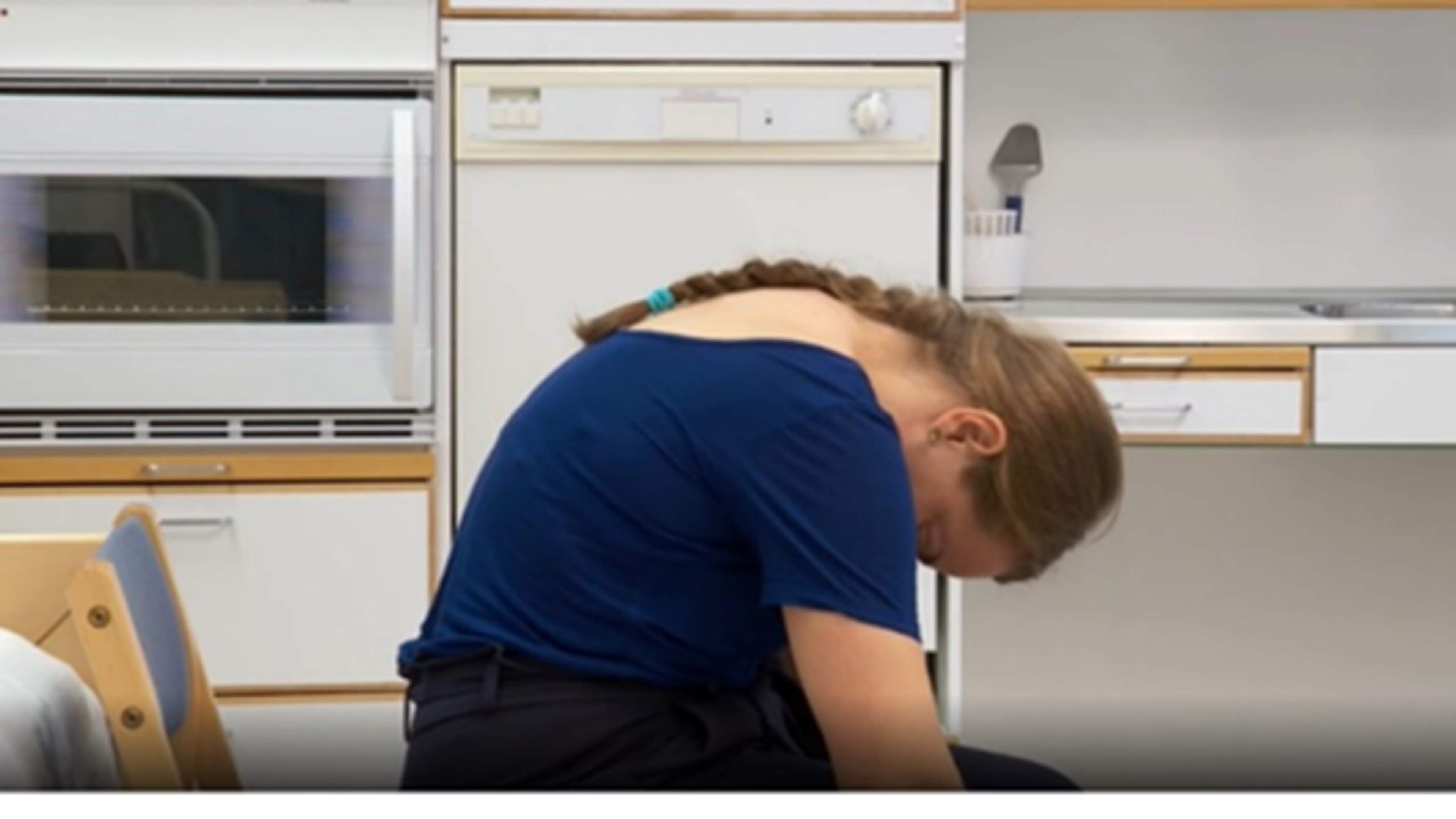 Nainen istuu ja pyöristää ylävartaloa eteenpäin.