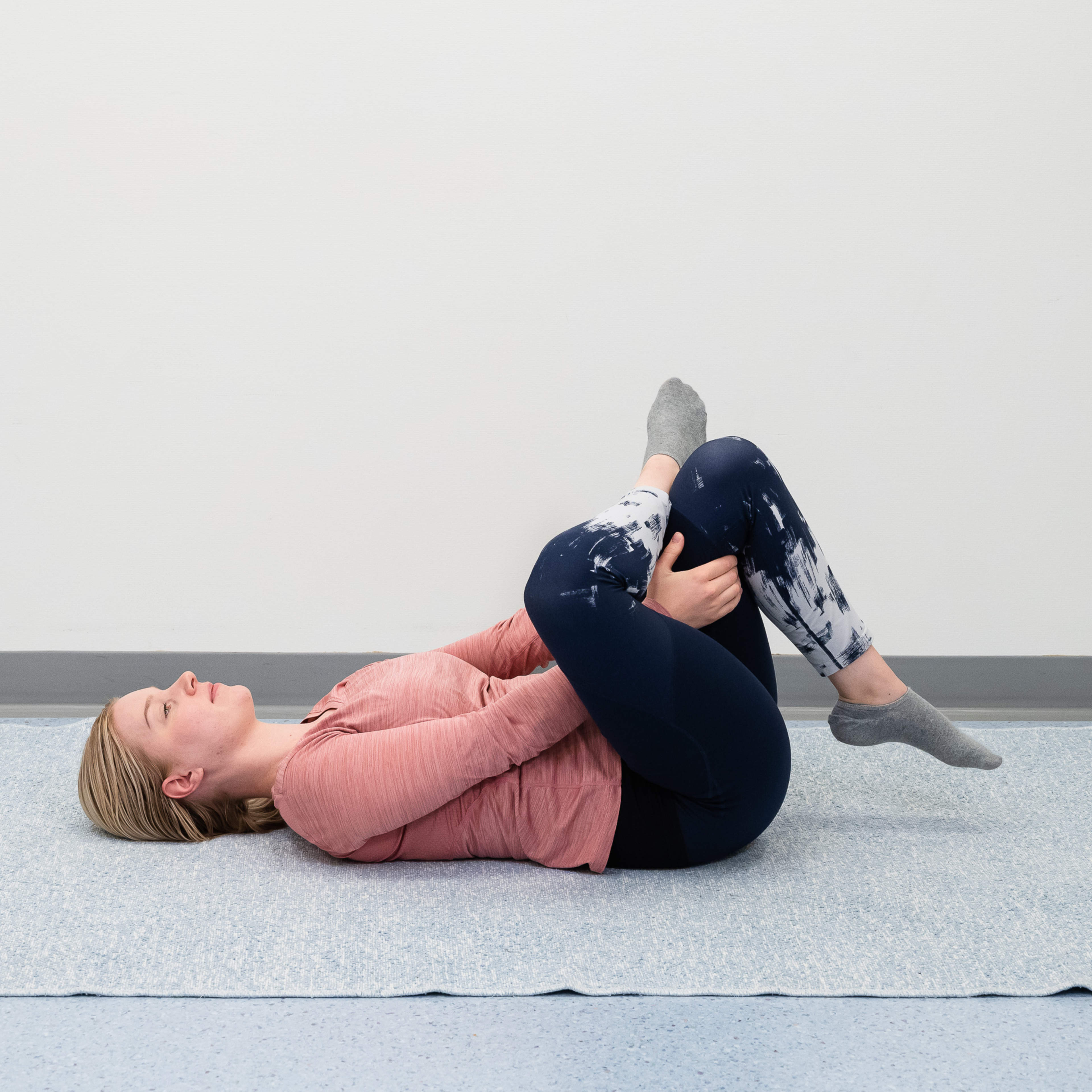 En kvinna ligger på golvet med höger vrist över vänster knä och stretchar sätesmuskeln.