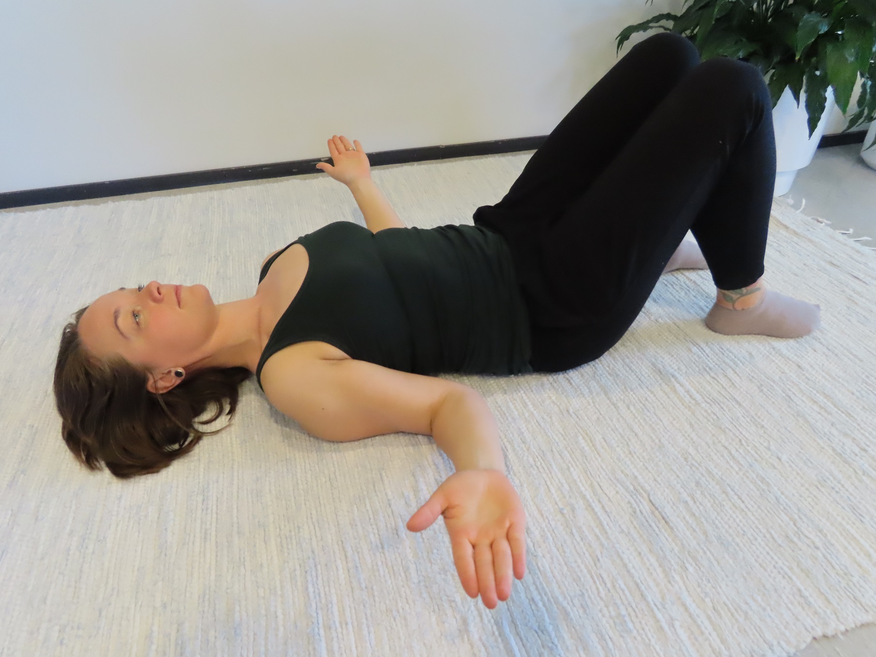 Kvinnan ligger på rygg på golvet, knäna böjda, armarna längs sidan av kroppen, armbågarna böjda och underarmarna öppnade ut åt sidorna.