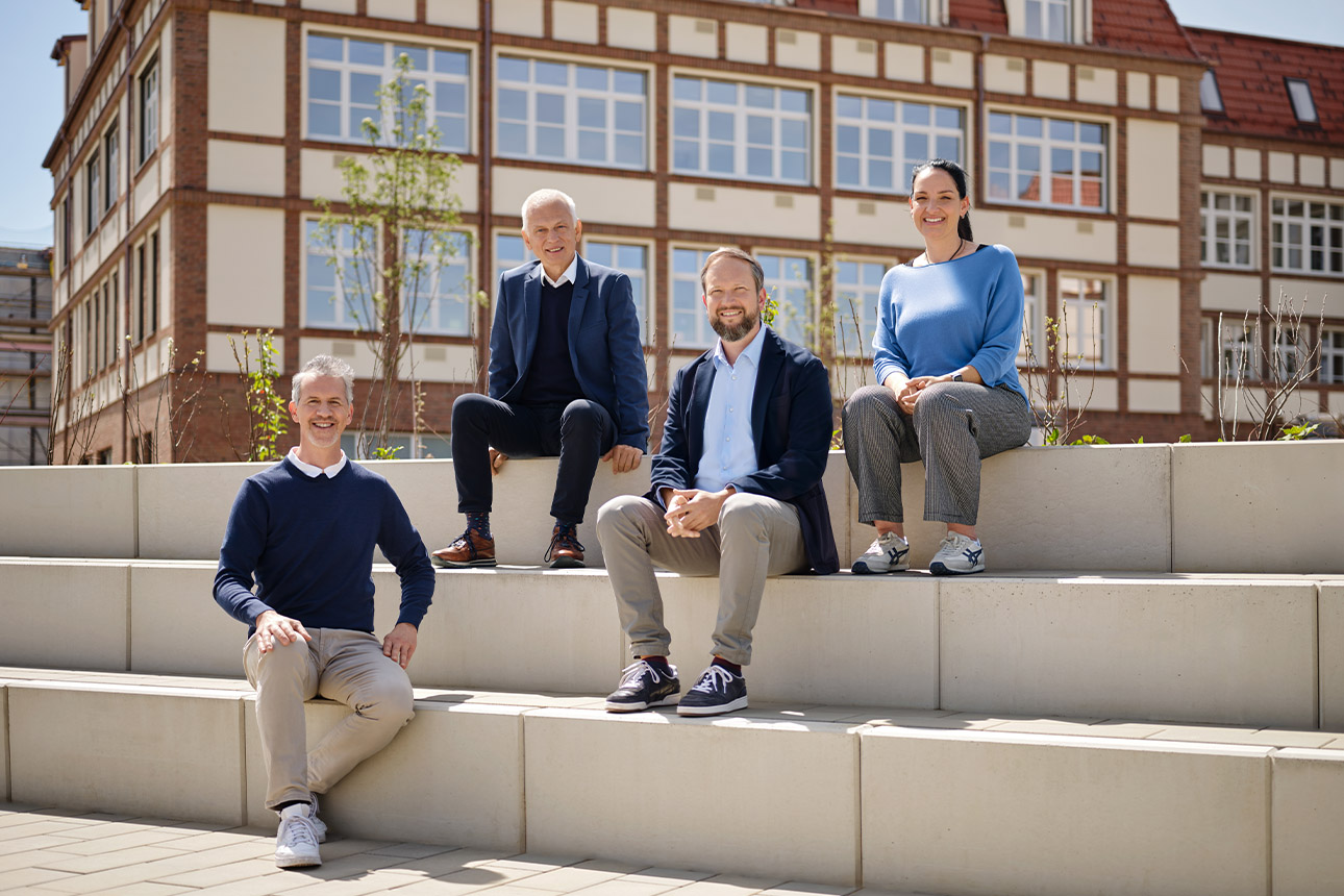 Kund*innen sitzen auf Stufen vor dem Schulgebäude