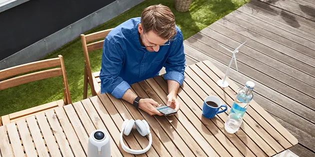 Ein Mann sitzt mit Smartphone in der Hand auf einer Terrasse.