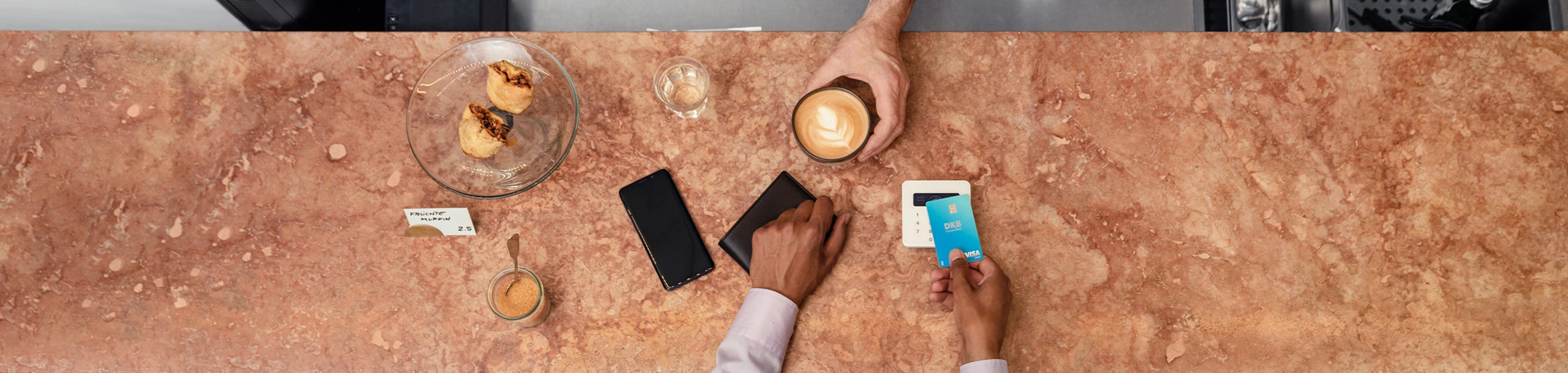 Eine Frau bezahlt ihren Kaffee mit der Visa Debitkarte der DKB