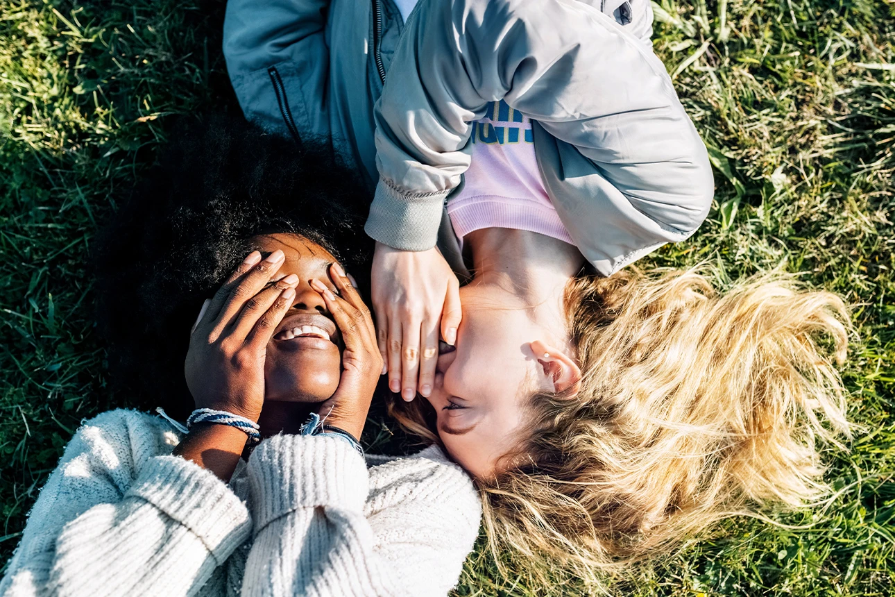 Zwei Frauen liegen auf einer Wiese und flüstern sich etwas ins Ohr