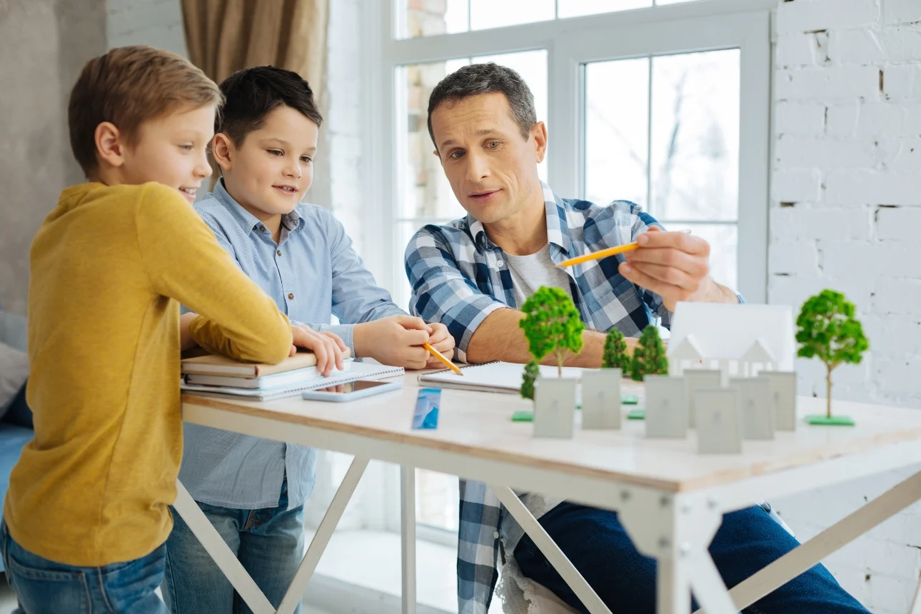 Ein Mann erklärt zwei Kindern anhand eines Modells den Energiebedarf eines Hauses