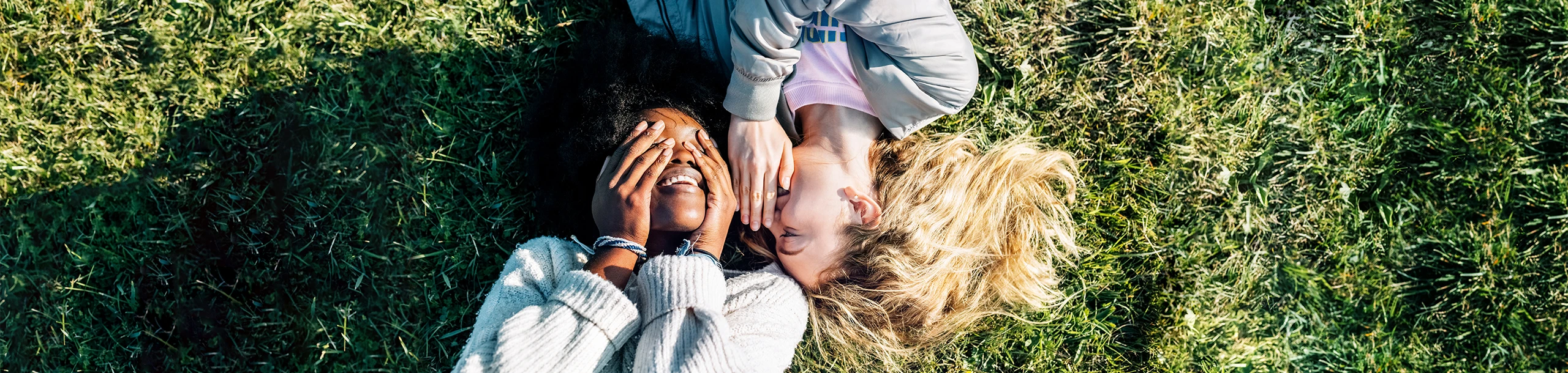 Zwei Frauen liegen auf einer Wiese und flüstern sich etwas ins Ohr