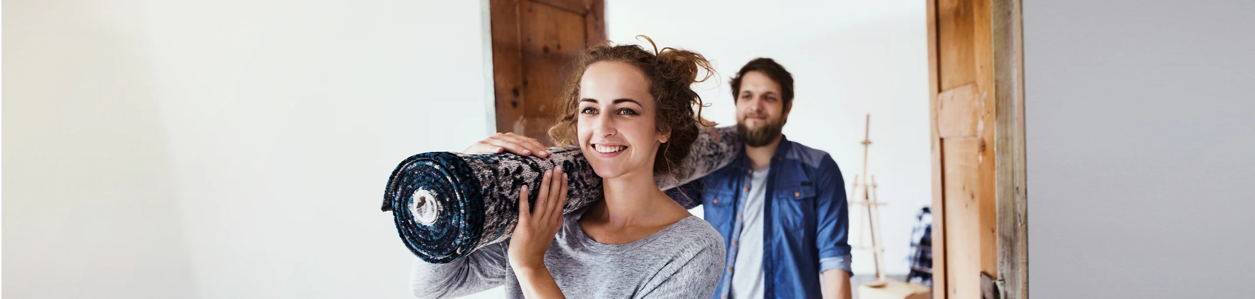 Eine Frau und ein Mann tragen gemeinsam einen Teppich in eine neue Wohnung