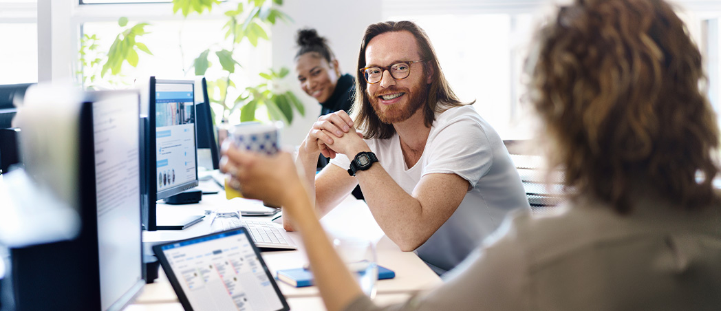 Zwei Frauen und ein Mann sitzen im Büro und unterhalten sich.