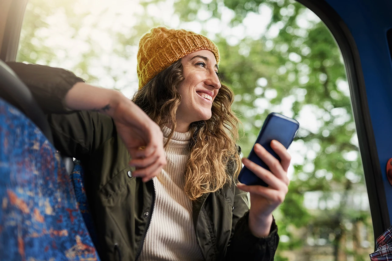 Eine lächelnde Frau mit Handy unterwegs mit dem Bus