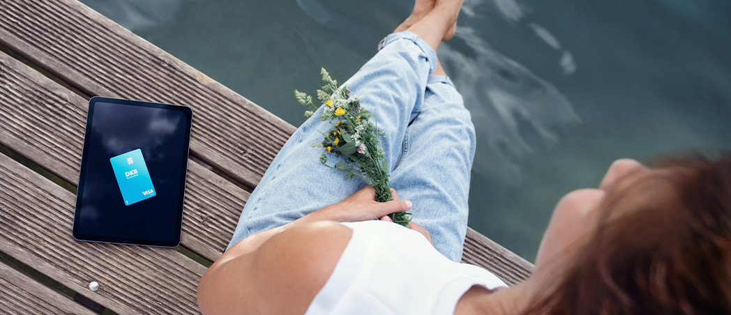 Foto einer Person, die am Rand eines Holzstegs am Wasser sitzt