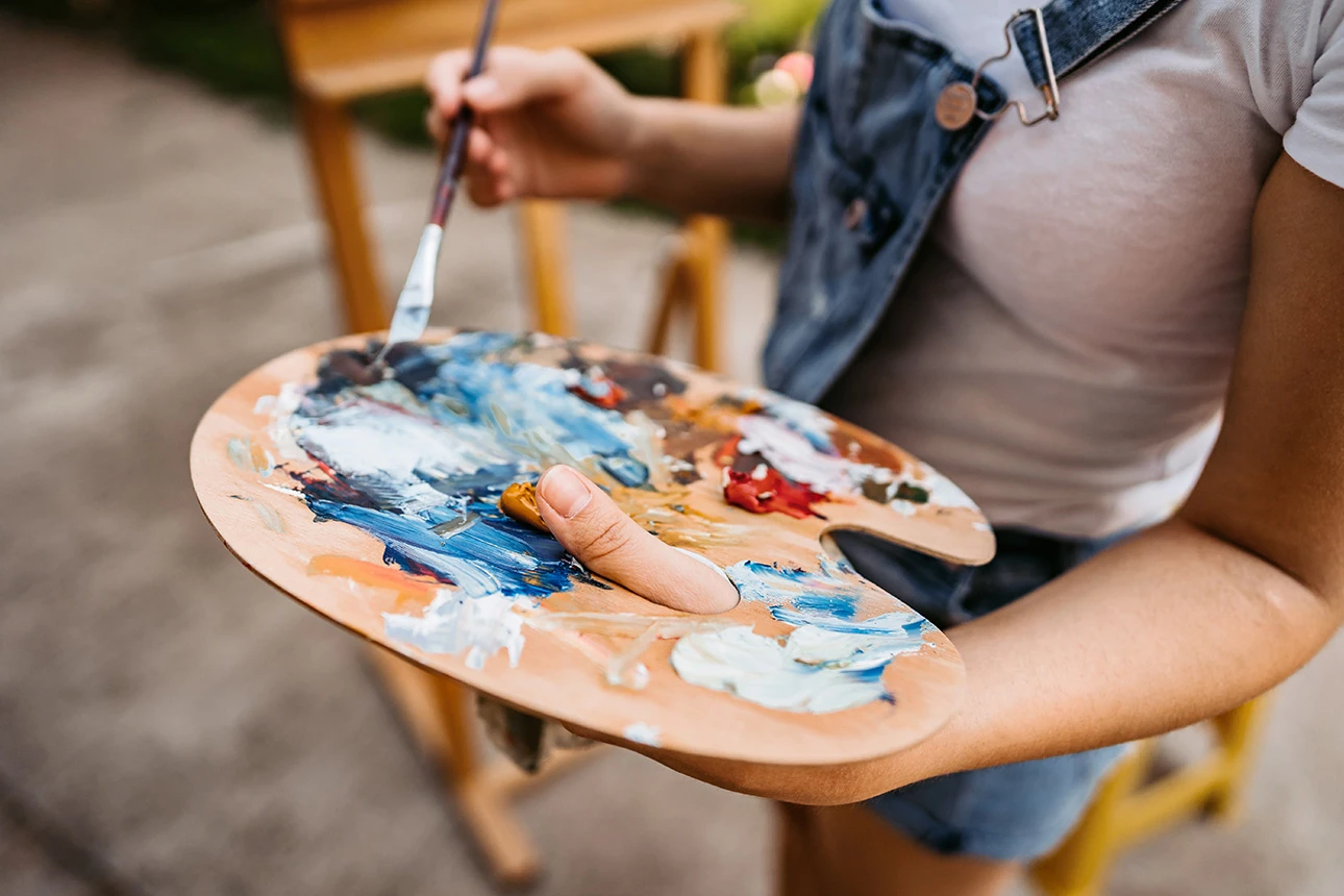 Eine Frau hält eine Mischpalette mit Farben und einem Pinsel in der Hand