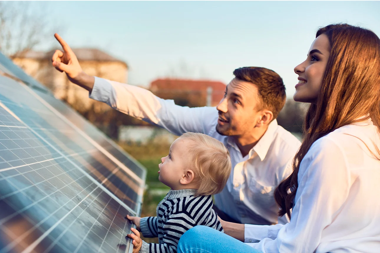 Eine dreiköpfige Familie sitzt vor einer Solaranlage