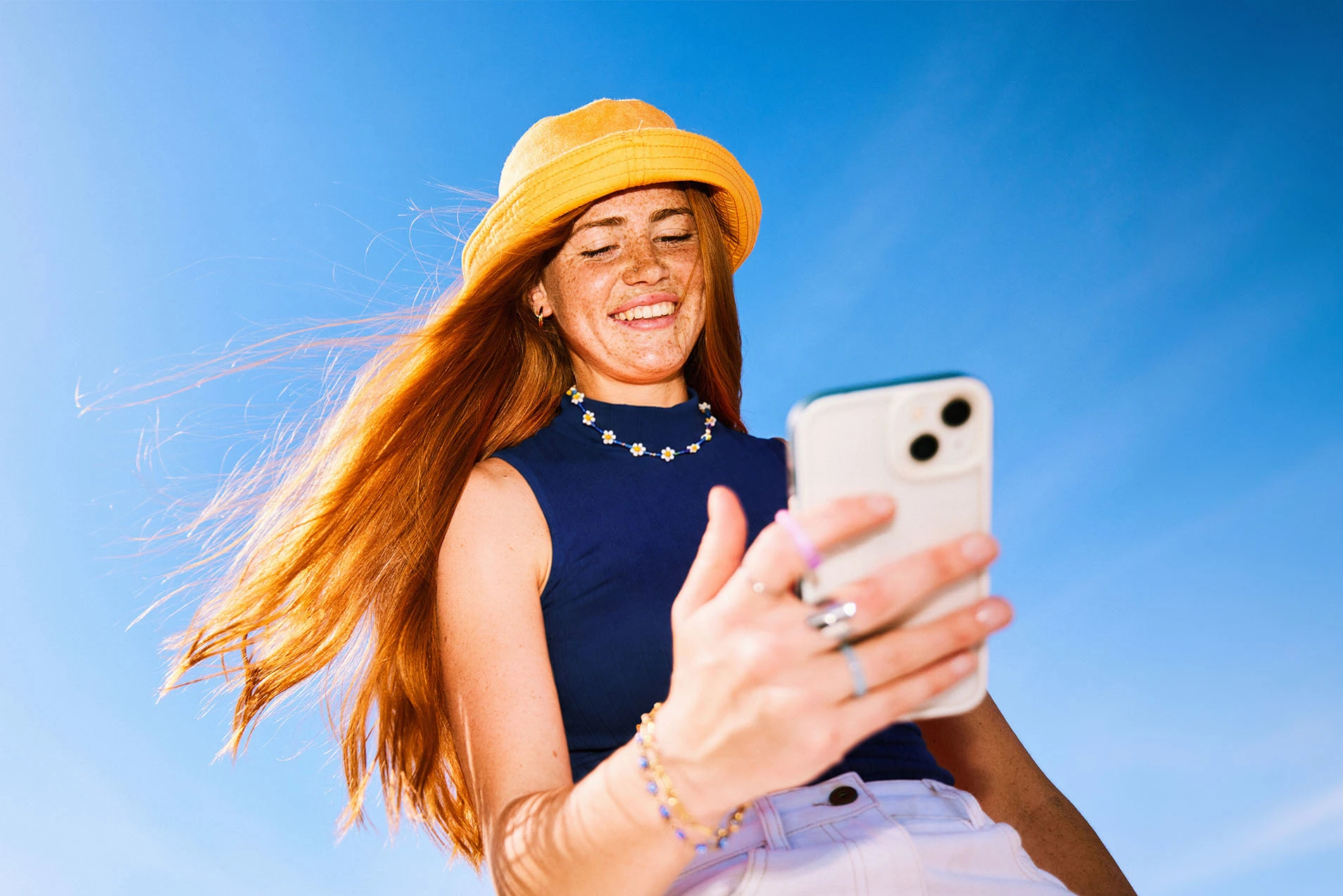 Lächelnde Frau mit Smartphone unter blauem Himmel