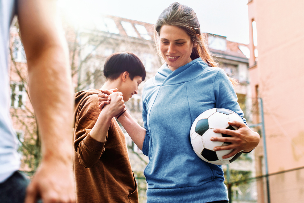 Frau mit Fußball gibt anderer Frau die Hand.