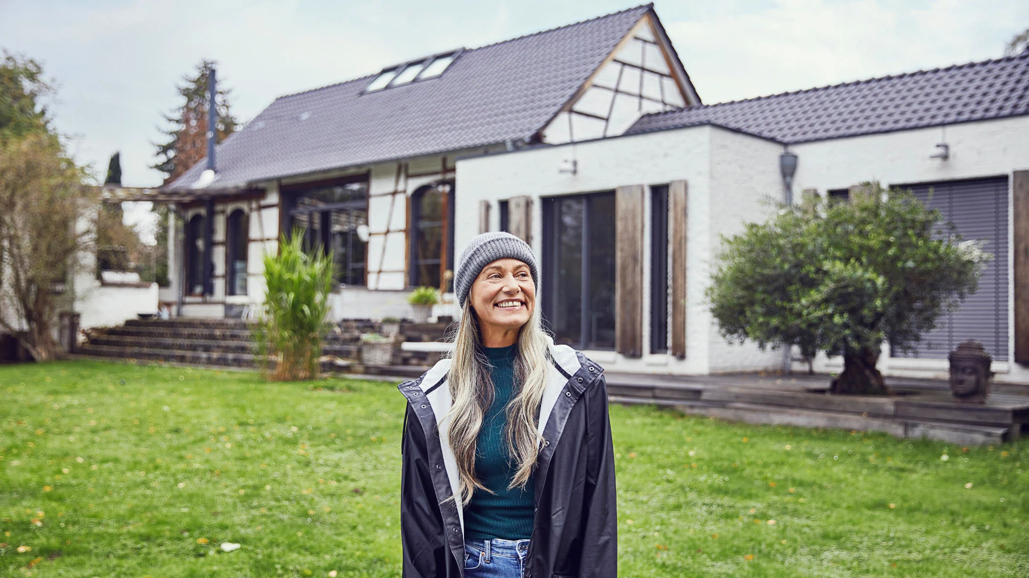 Eine Frau steht lächelnd vor einem Haus.