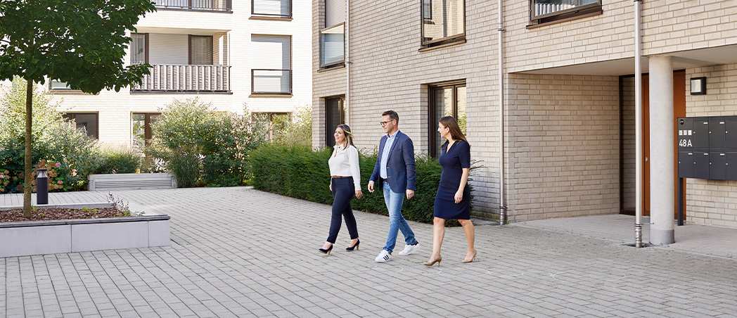 3 Personen überqueren Vorplatz eines verwalteten Gebäudes