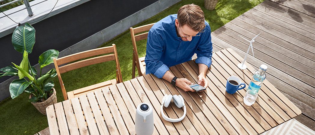 Ein Mann sitzt mit Smartphone in der Hand auf einer Terrasse