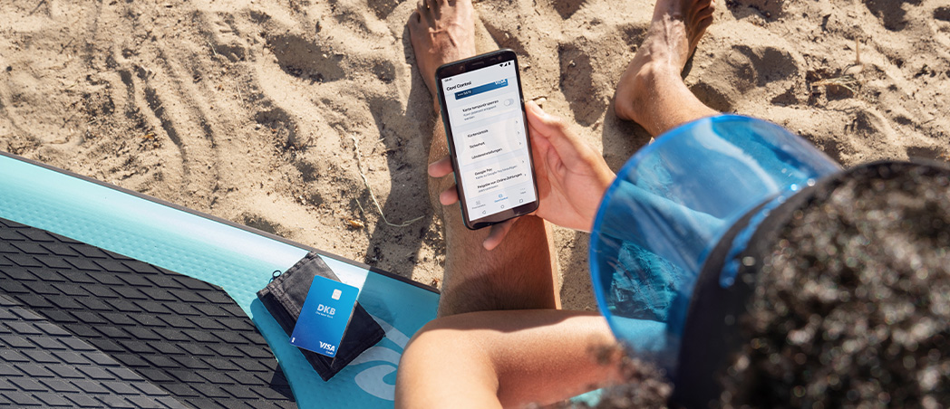 Person mit Smartphone und DKB Visa Card am Strand