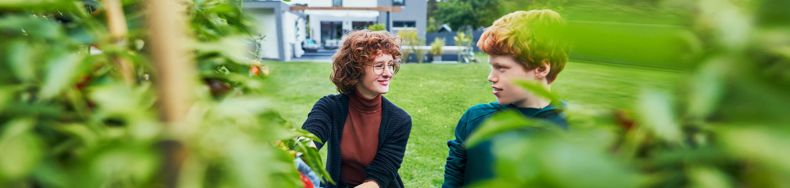 Frau mit Kind sind glücklich im Garten Ihres Hauses - finanziert mit der nachhaltigen Baufinanzierung der DKB.