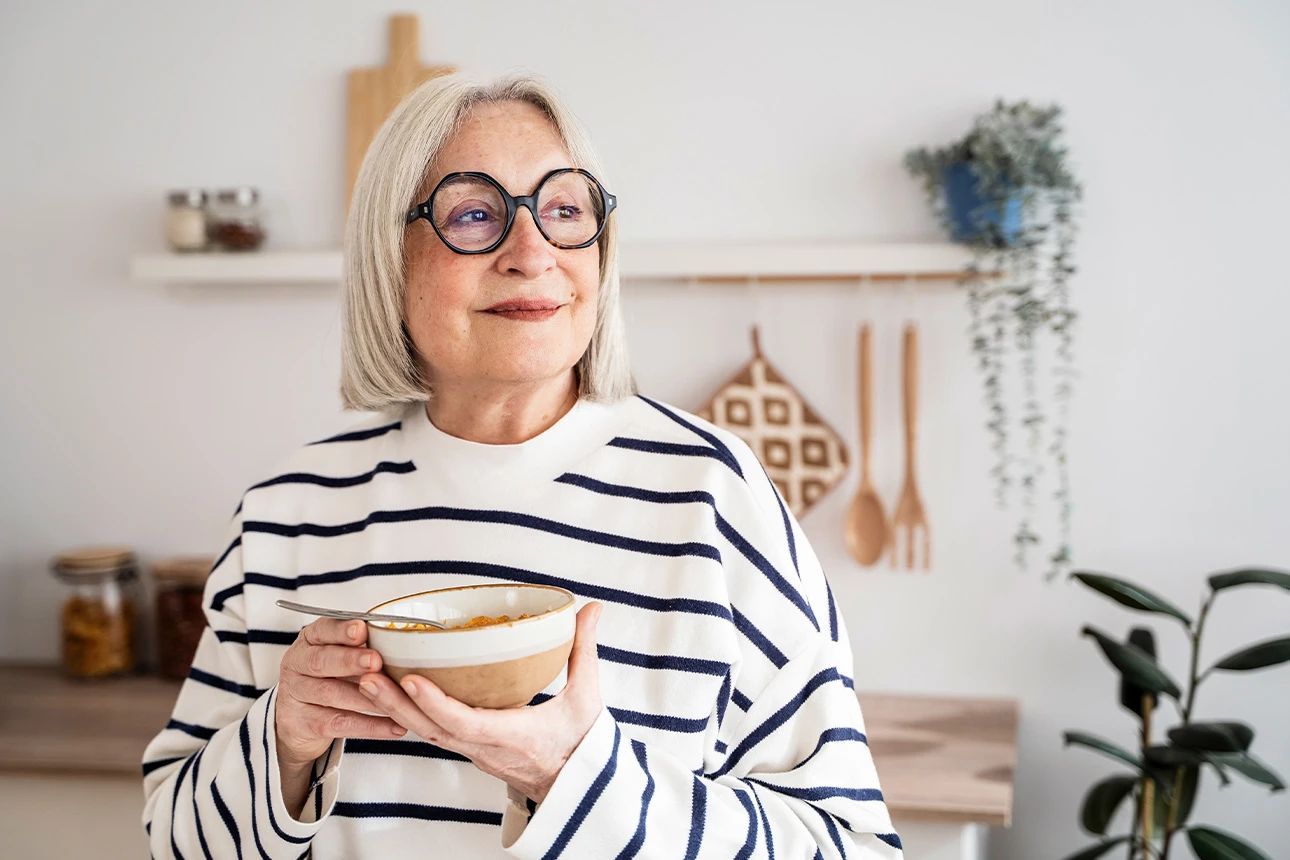 Seniorin genießt Essen in heller Küche, lächelnd und entspannt